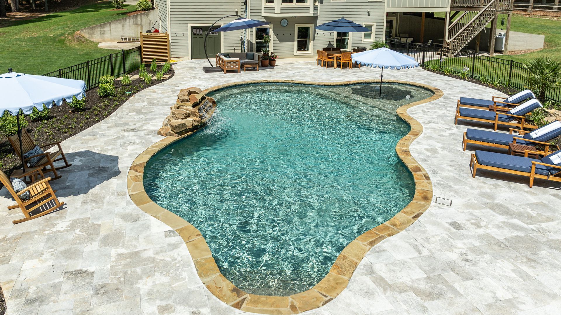 Backyard swimming pool with stone deck, lounge chairs, and a small patio area