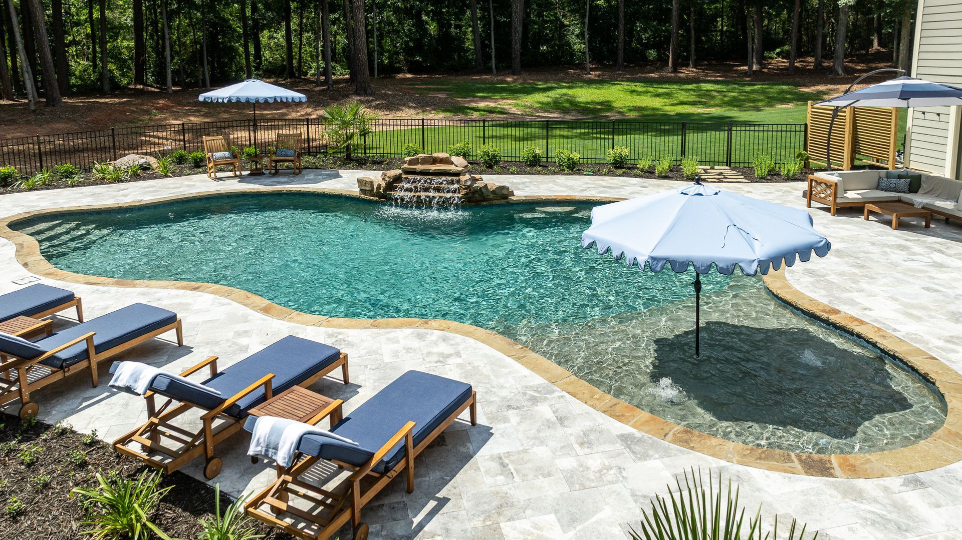 Backyard pool with turquoise water, stone patio, lounge chairs, and white umbrellas surrounded by trees