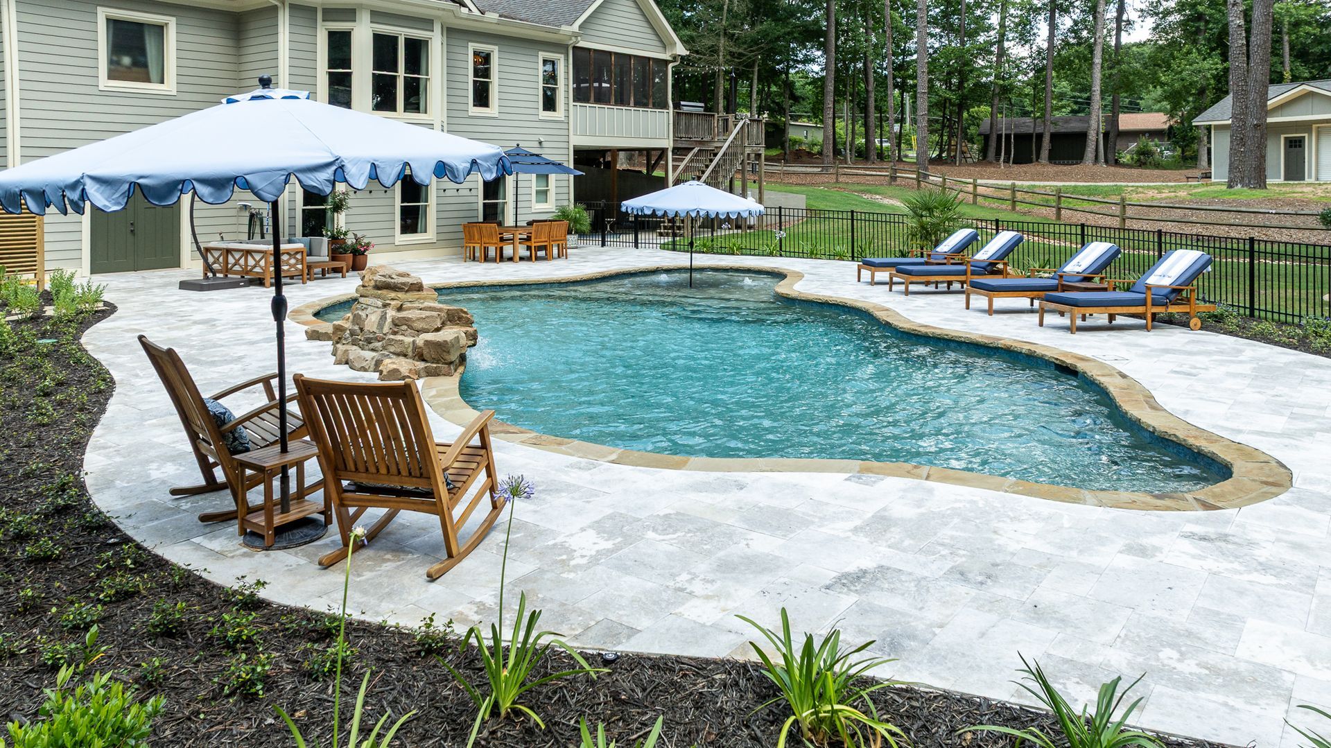 Backyard pool with lounge chairs, umbrellas, and stone patio beside a house