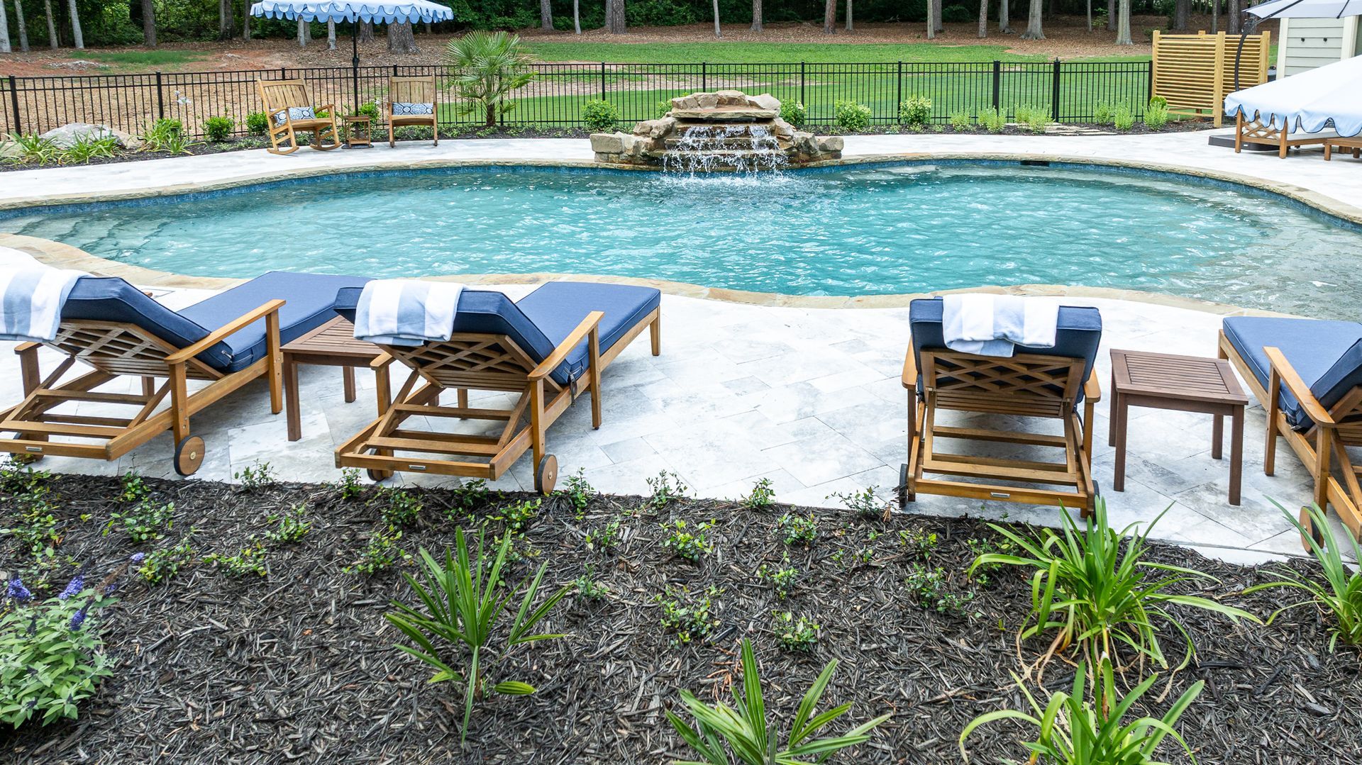 Backyard pool with wooden lounge chairs on a patio and landscaped garden border