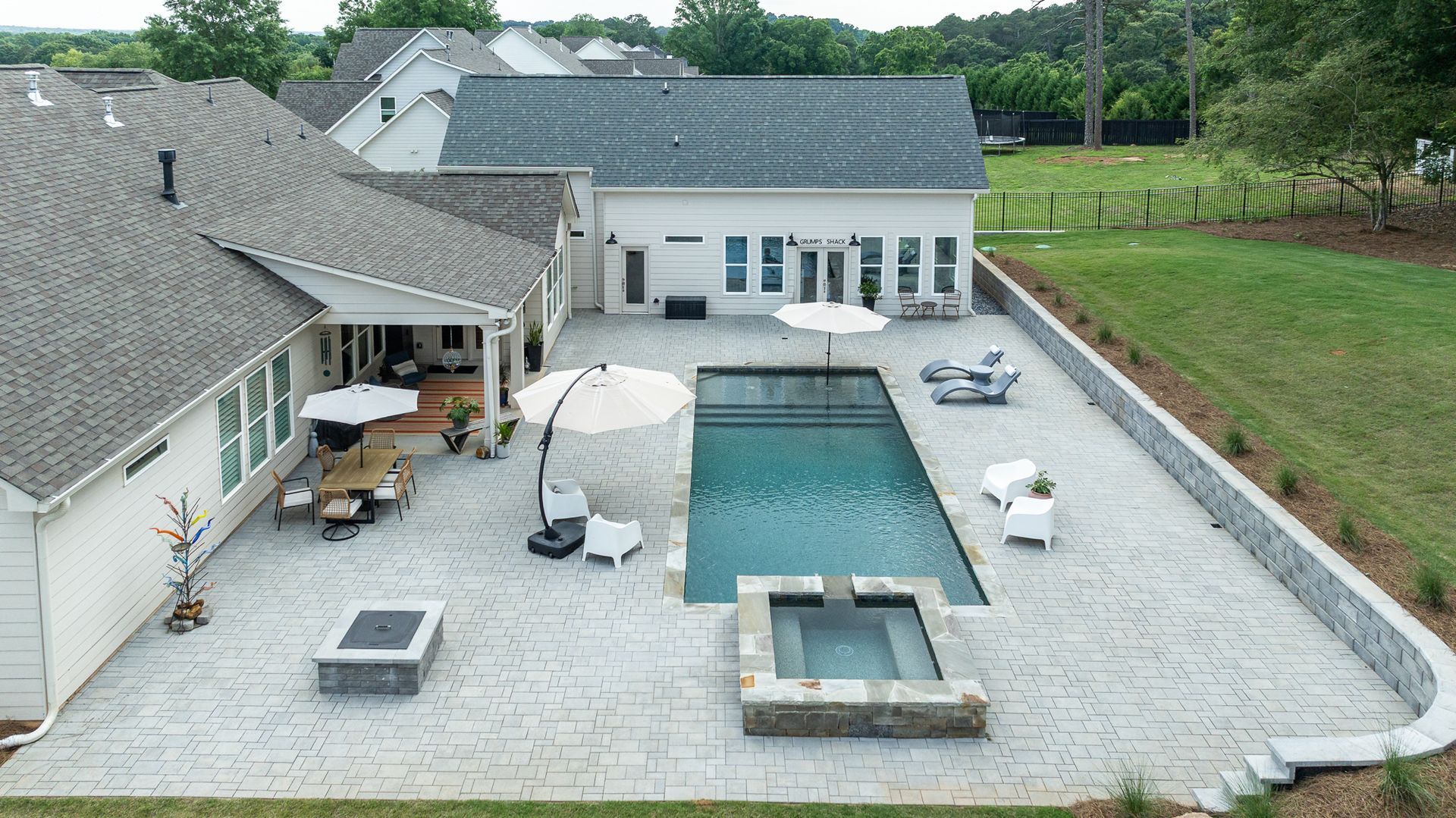 Backyard with rectangular pool, stone patio, lounge chairs, umbrella, and modern house with screened porch