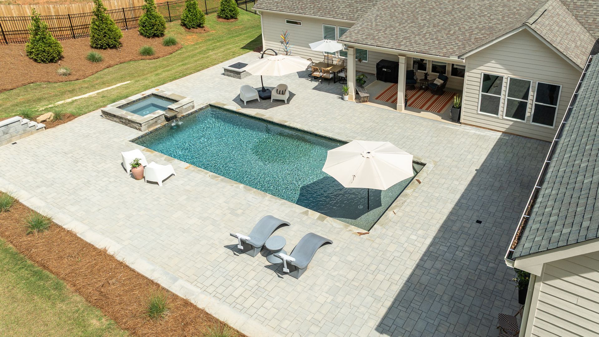 Backyard patio with a rectangular pool, lounge chairs, and a house with covered seating area
