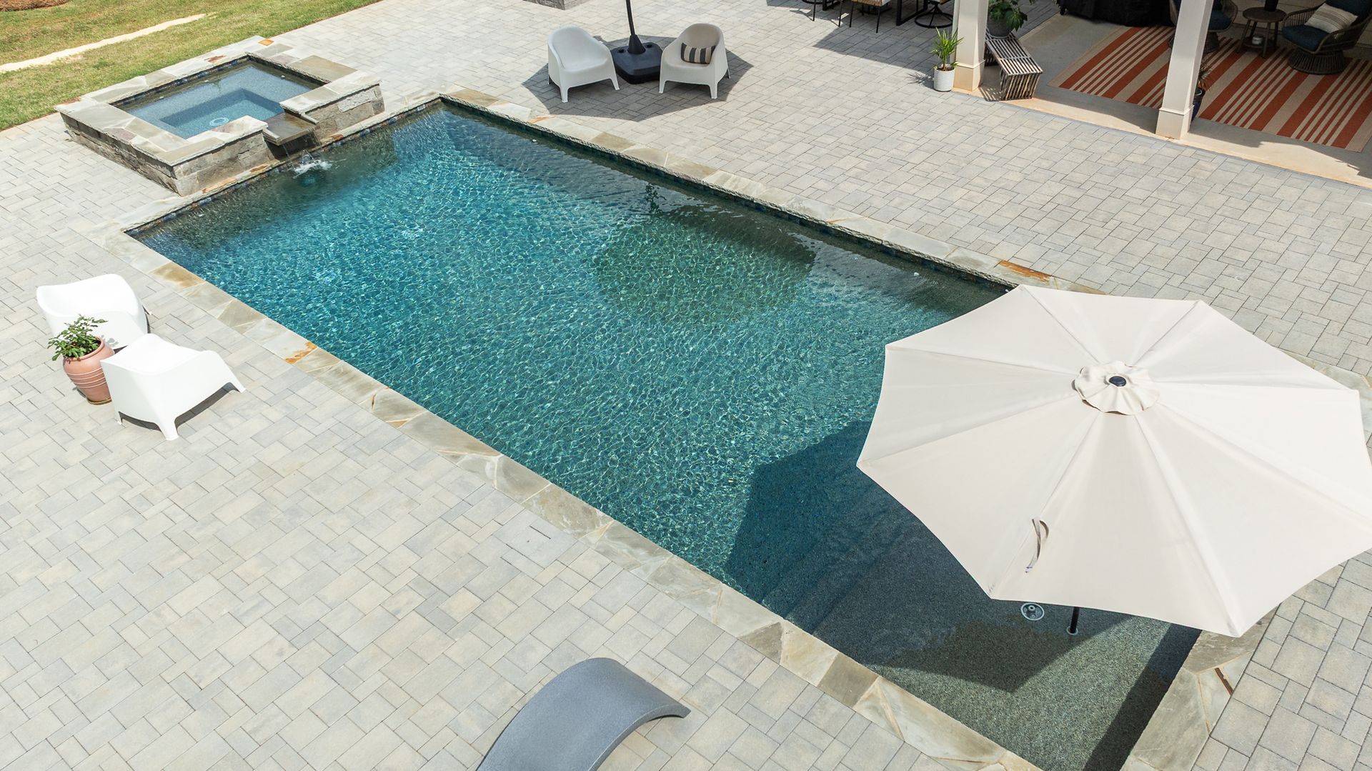 Aerial view of a rectangular backyard swimming pool with white lounge chairs and a patio umbrella