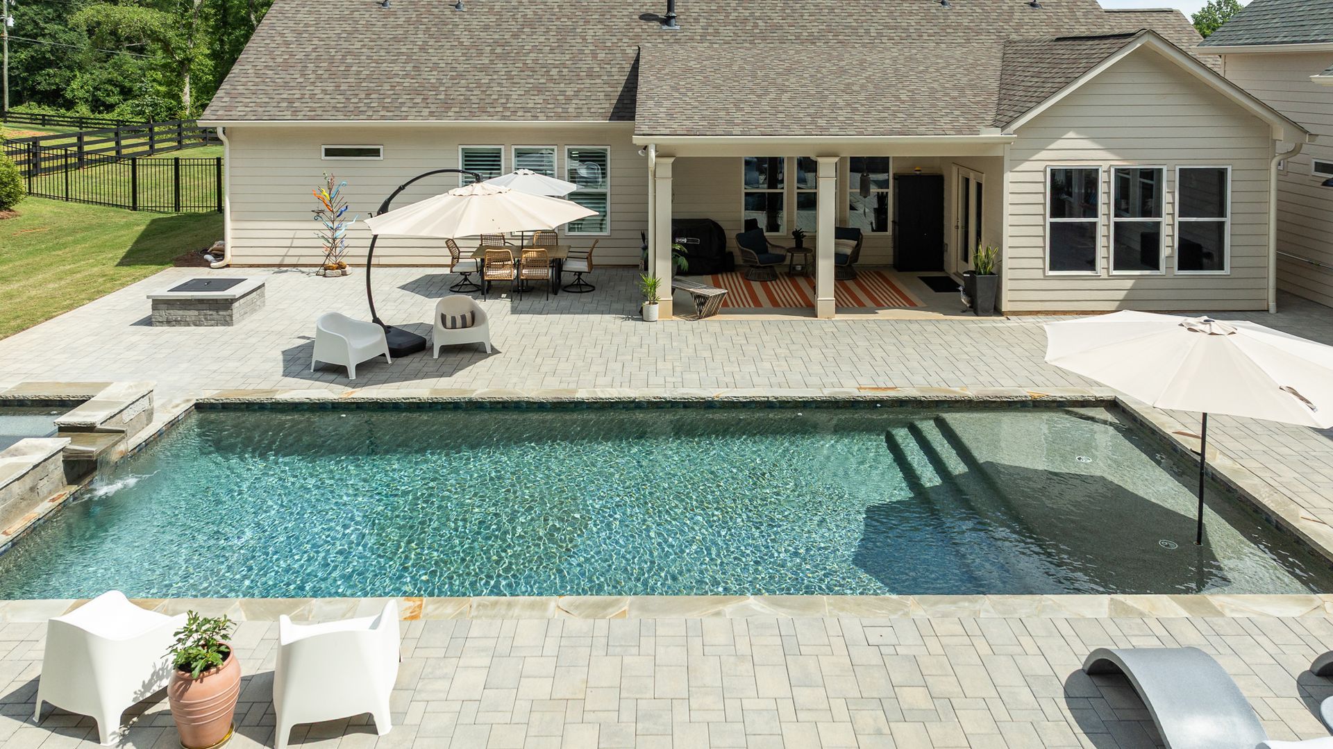 Backyard pool with glass fence, patio, lounge chairs, and a house in the background