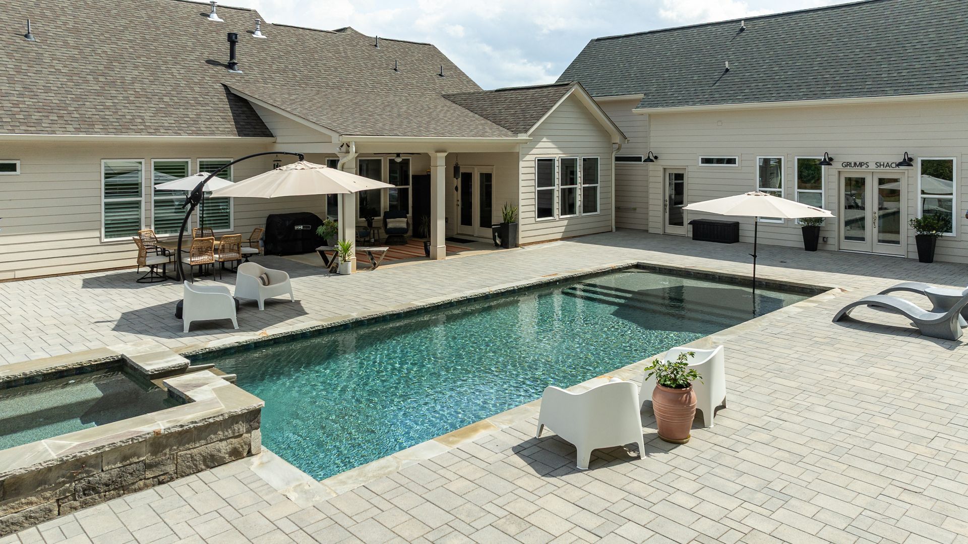 Modern backyard with a turquoise pool, stone patio, lounge chairs, umbrellas, and a house in the background
