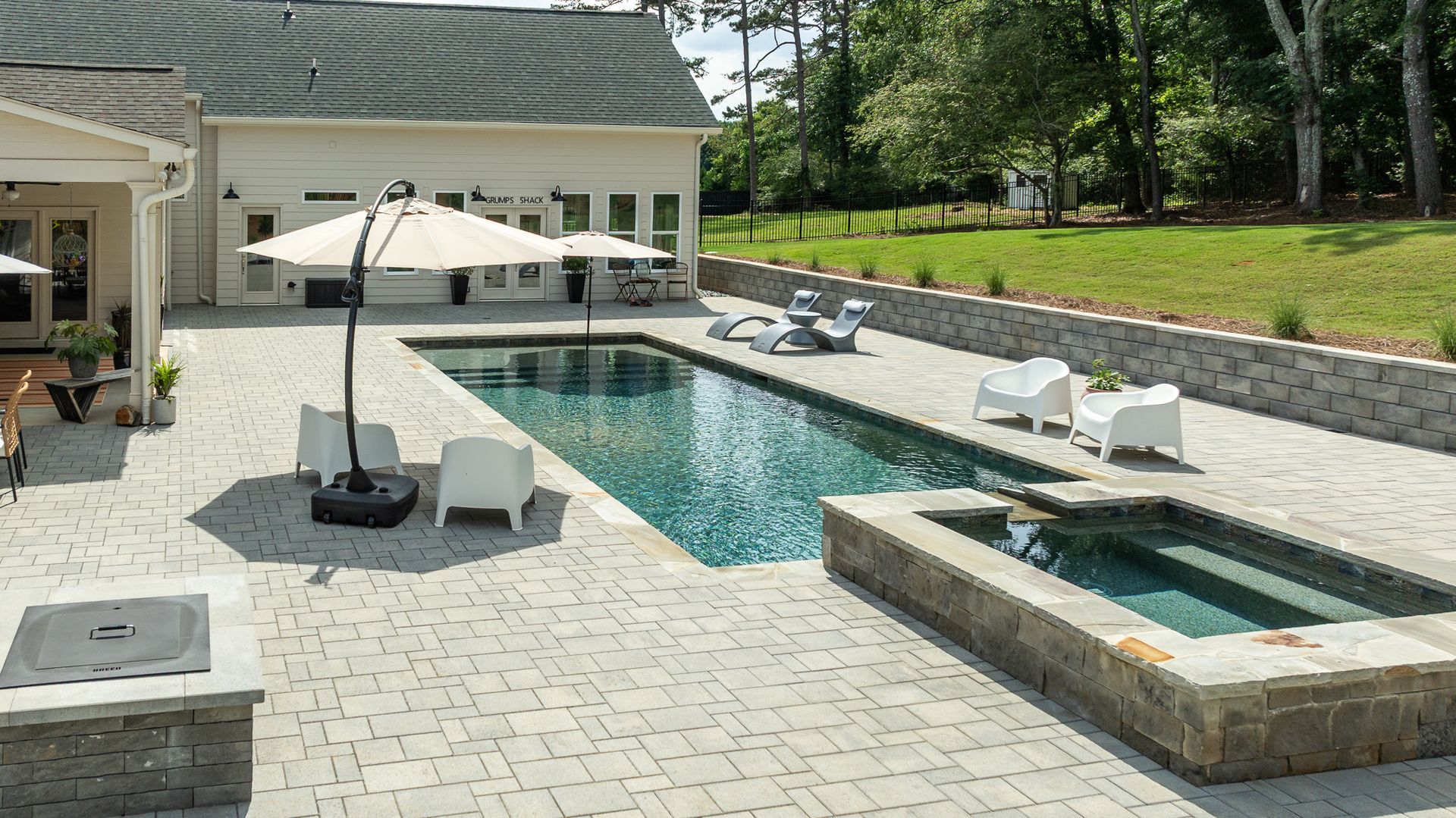 Modern backyard patio with a swimming pool, hot tub, umbrella, and lounge chairs