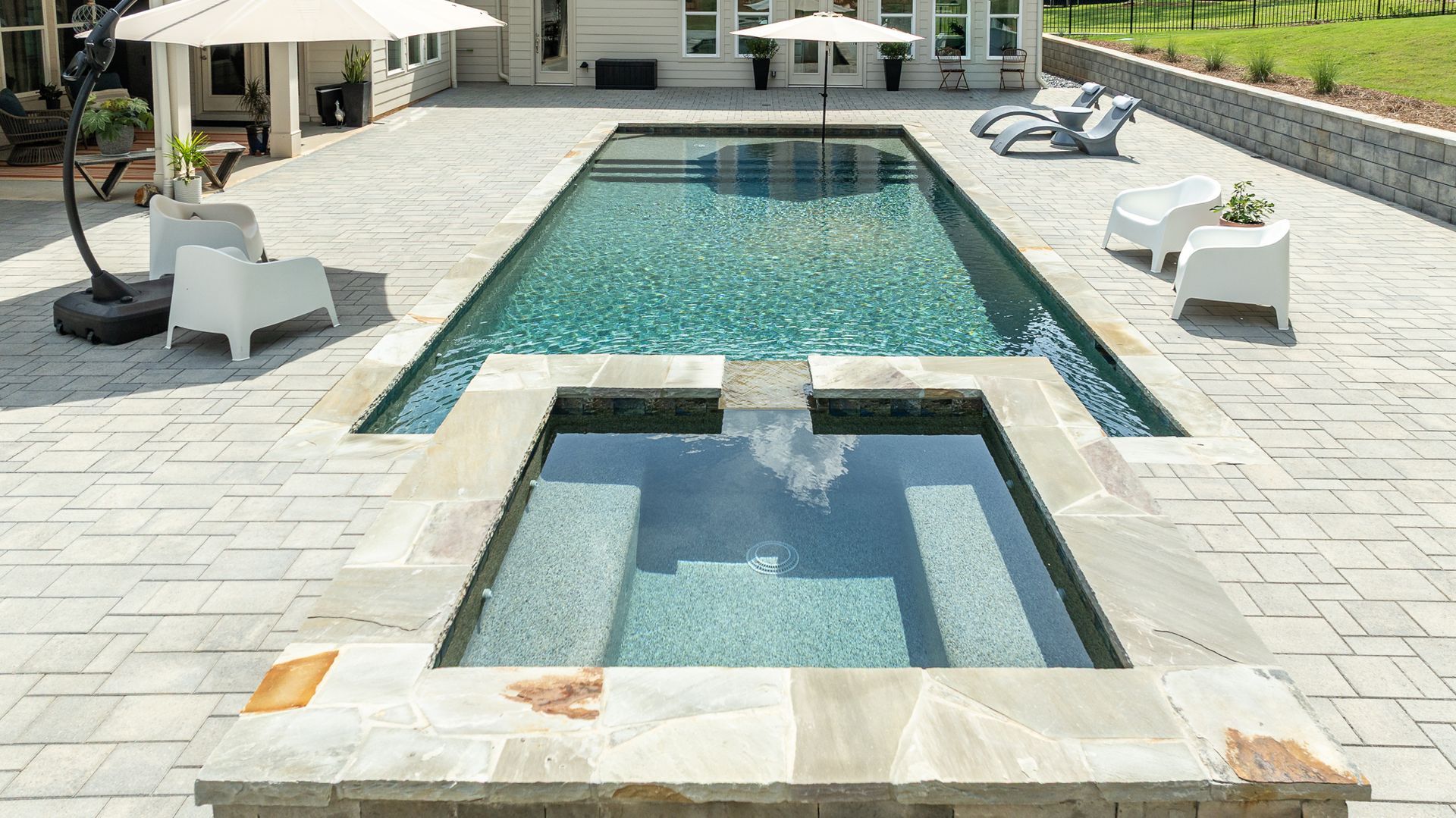 Modern backyard pool with a raised spa and lounge chairs on a stone patio
