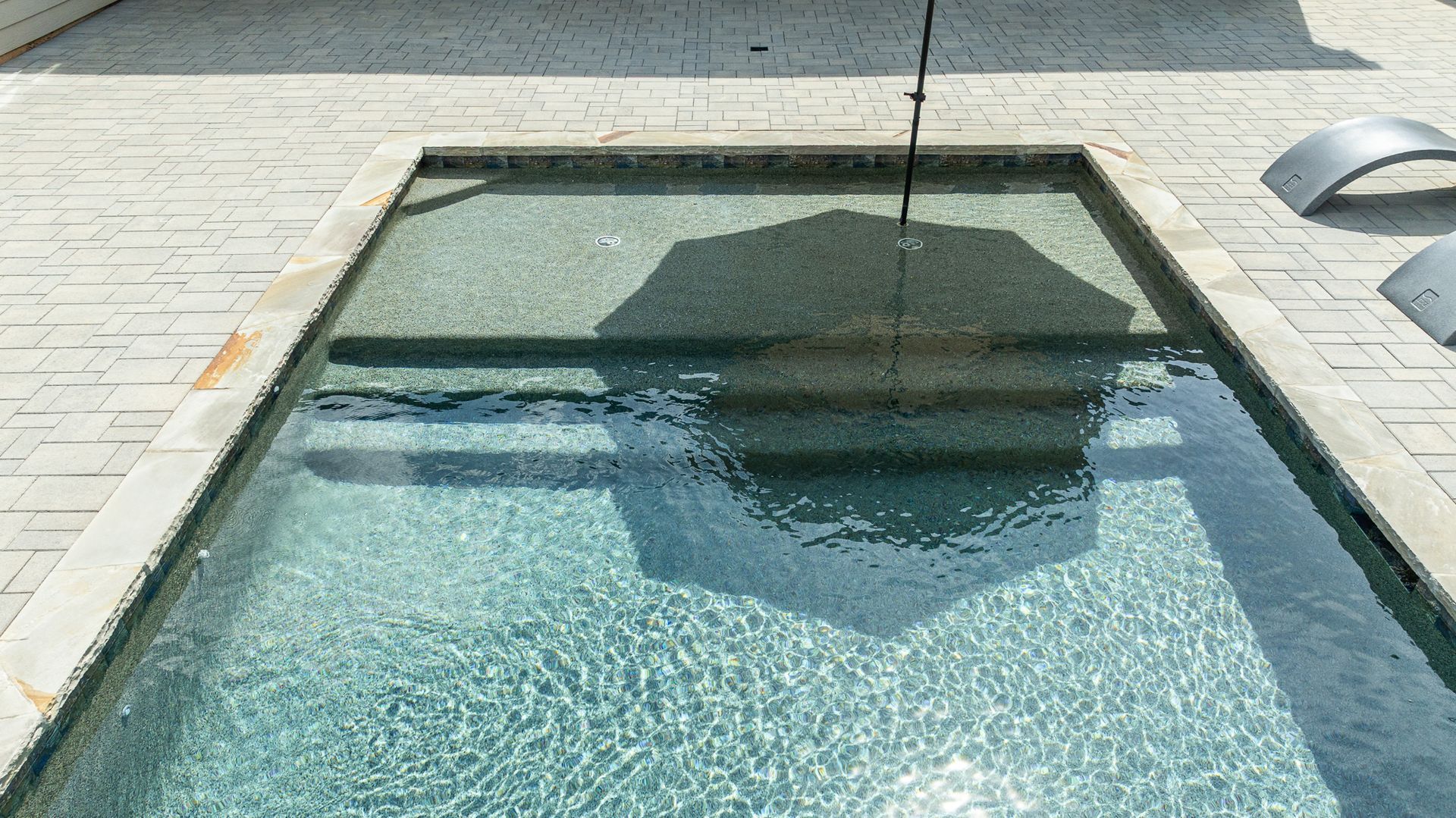 Rectangular outdoor pool with clear blue water and a dark reflection of a nearby tree