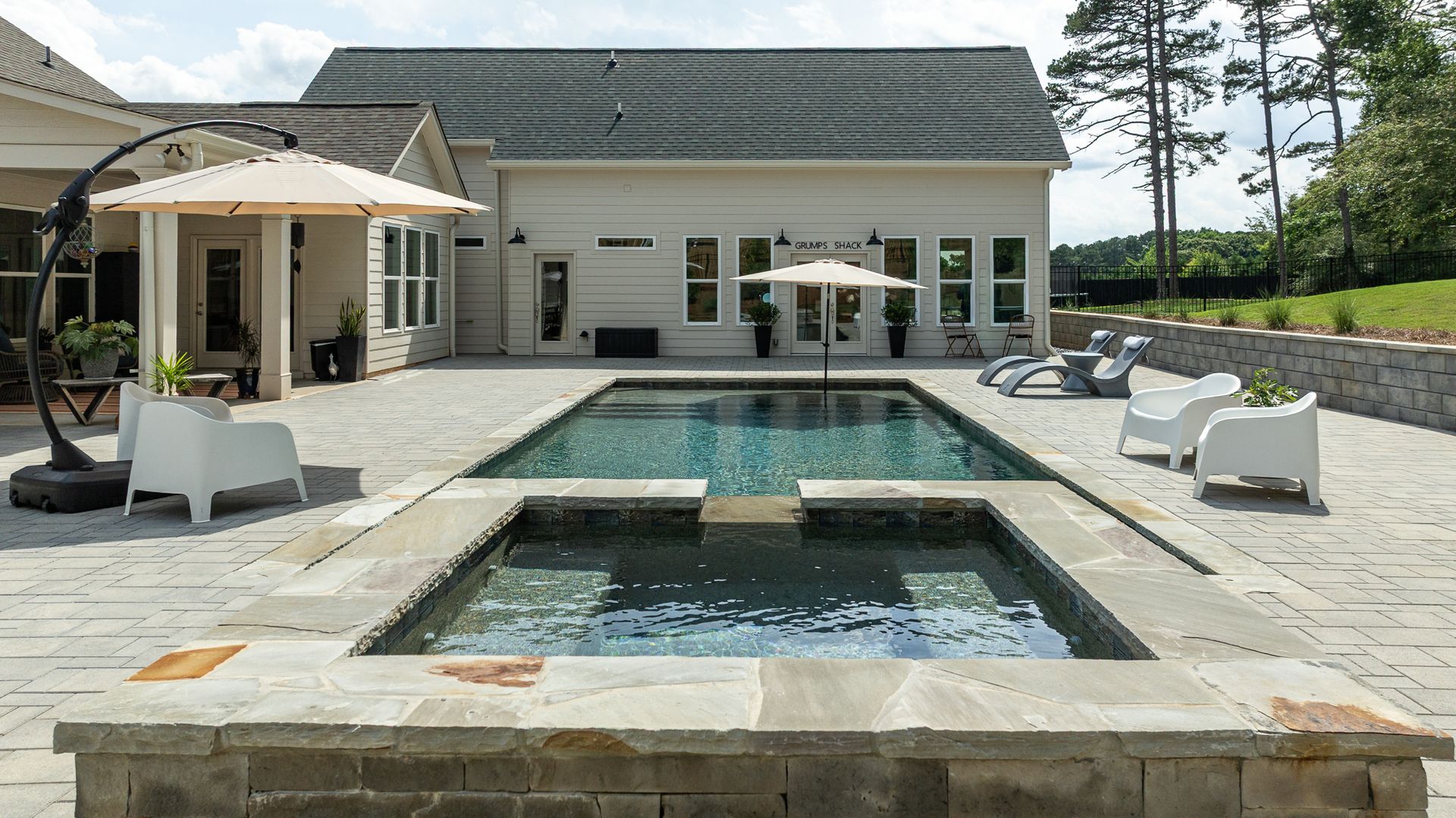 Modern backyard with a large pool, hot tub, lounge chairs, and a white house in the background
