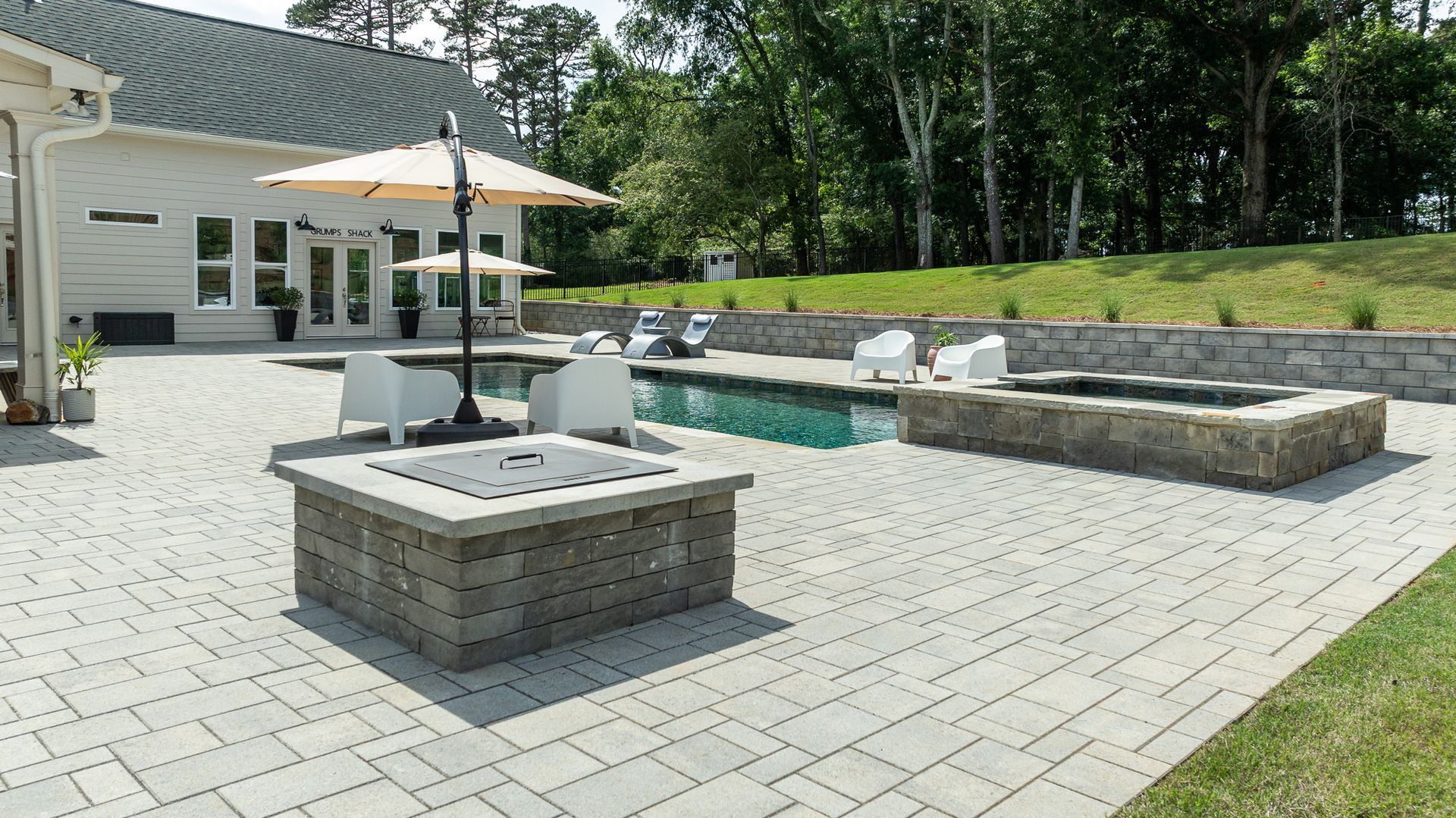 Patio with stone fire pit, umbrella table, lounge chairs, and a swimming pool beside a house