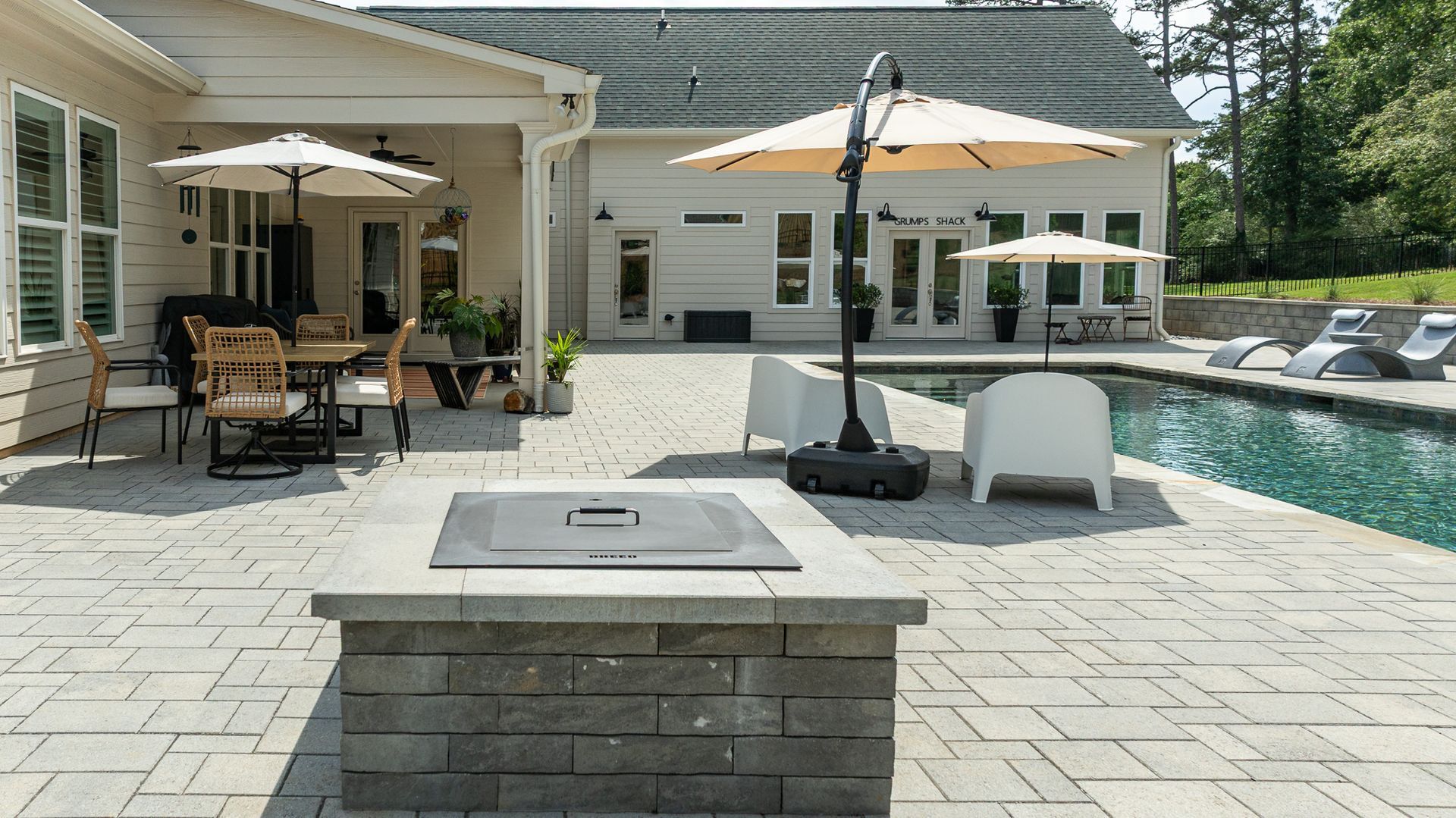 Backyard patio with pool, outdoor seating, fire pit, and umbrella beside a house