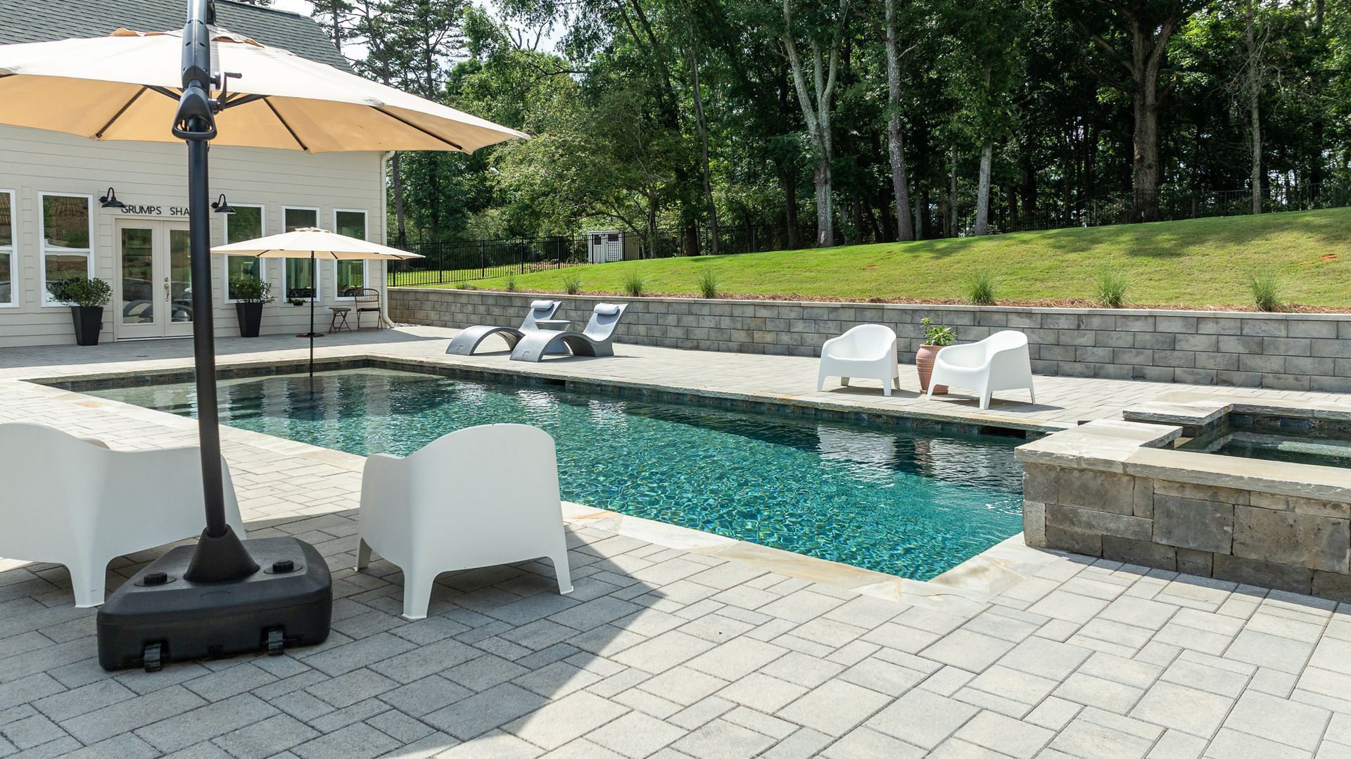 Backyard pool with lounge chairs, white umbrella, and stone patio beside a modern house