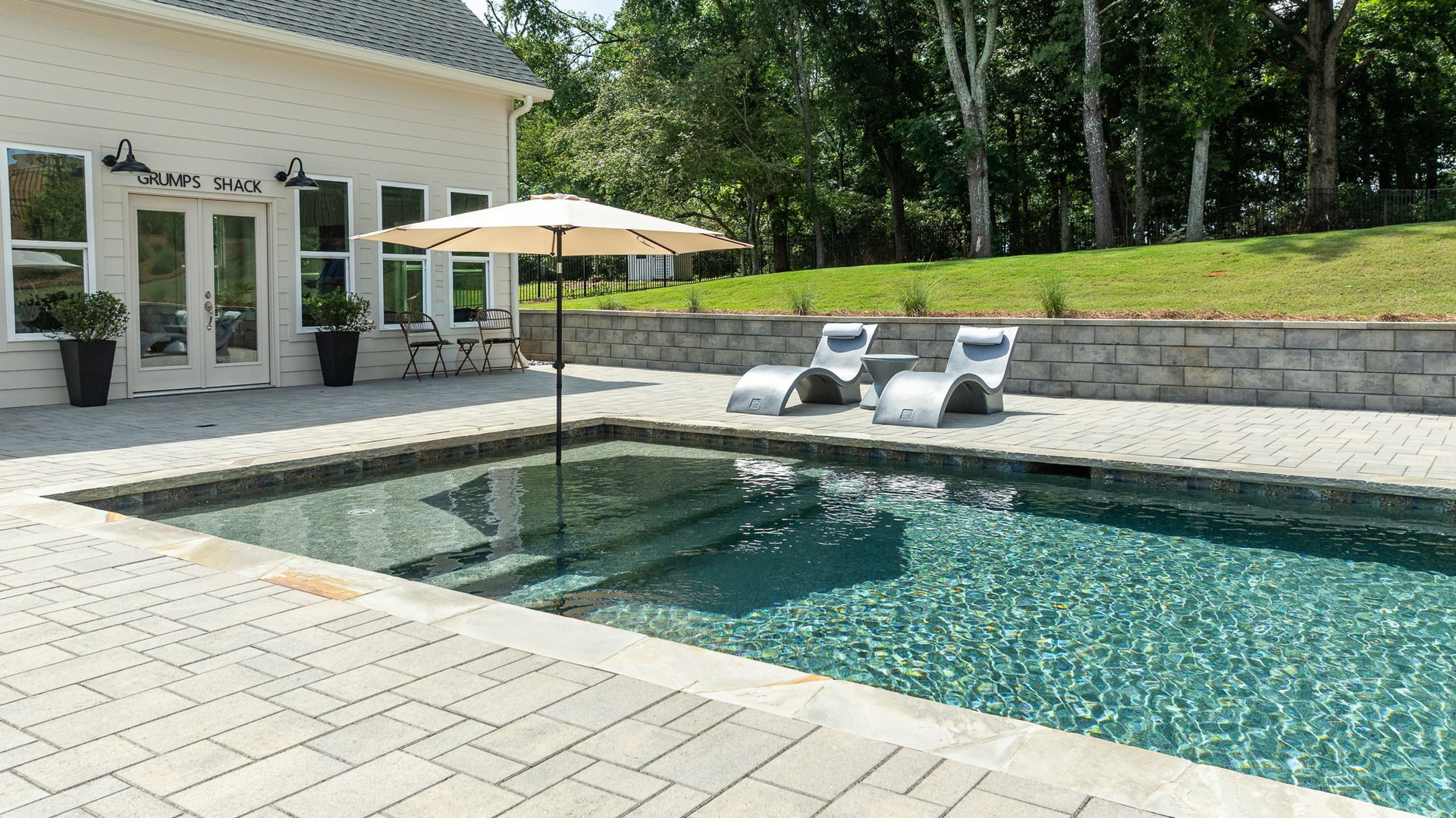 Backyard patio with a rectangular swimming pool, lounge chairs, and a patio umbrella beside a house