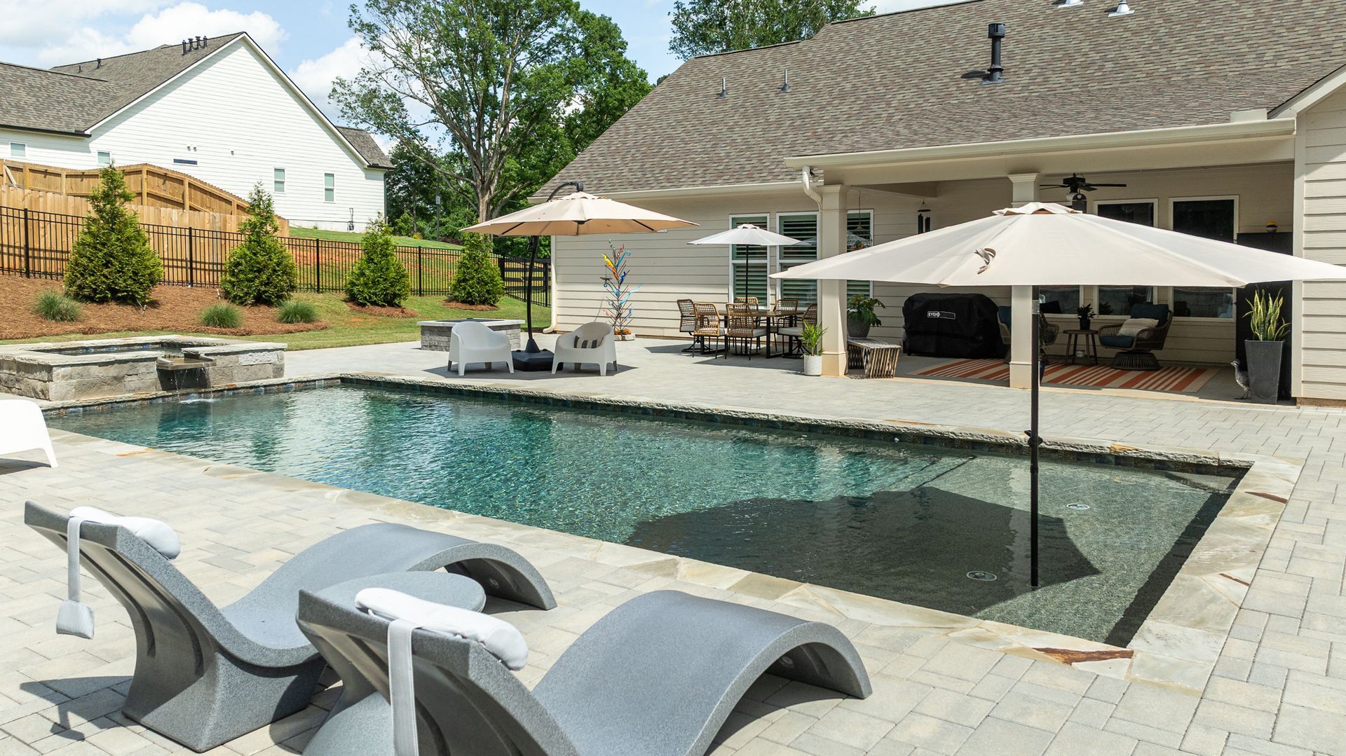Backyard pool with lounge chairs, umbrellas, and a patio beside a modern home