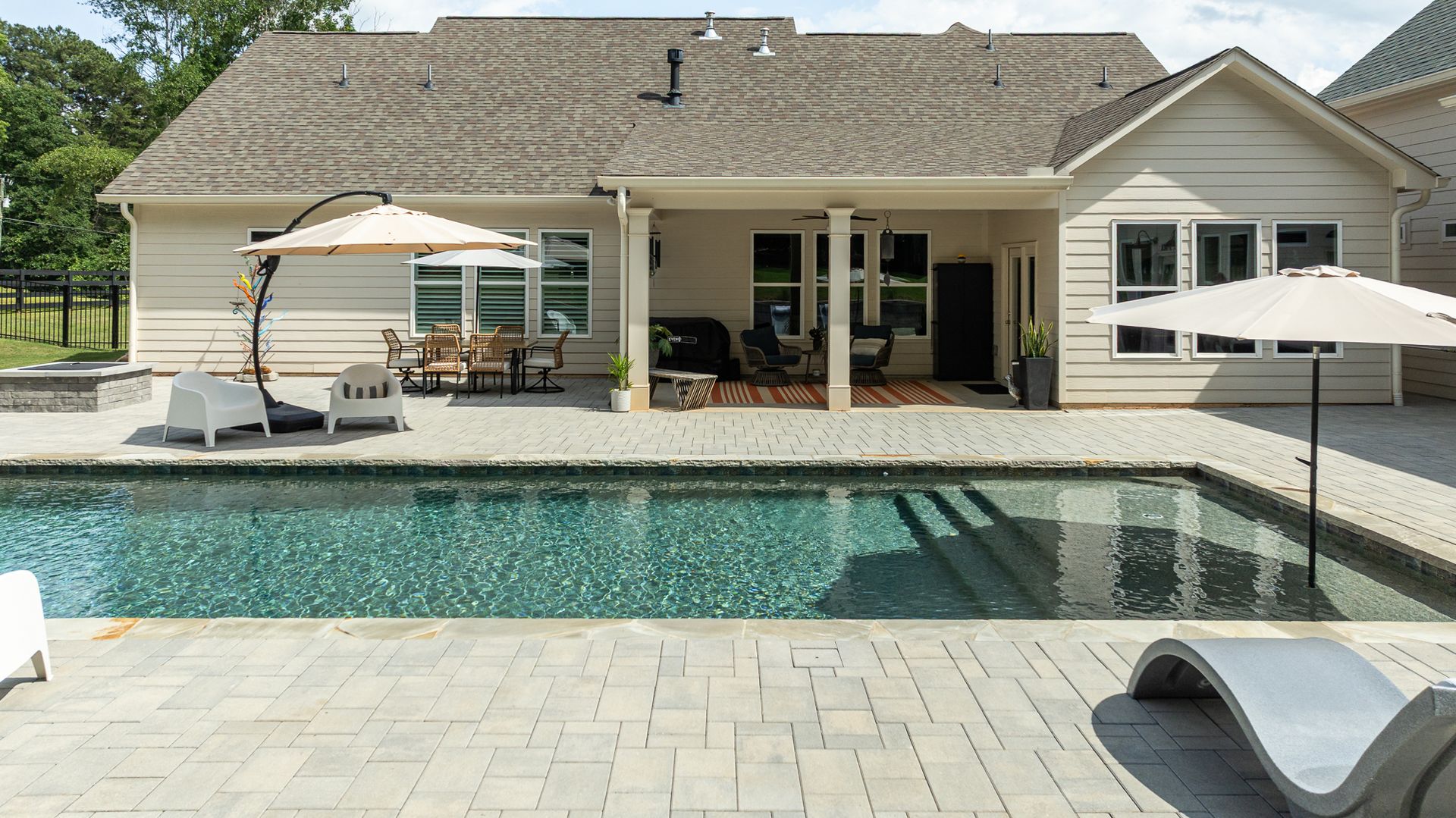Backyard pool with patio, lounge chairs, umbrellas, and a house in the background