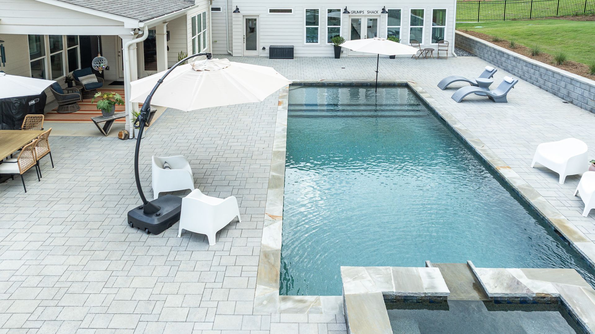 Backyard patio with a rectangular swimming pool, lounge chairs, and a covered seating area.