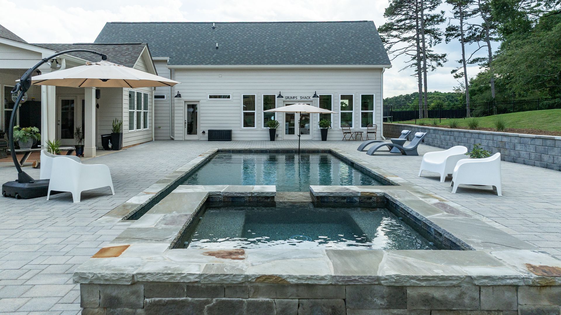 Modern house patio with a pool and hot tub, white lounge chairs, and stone deck