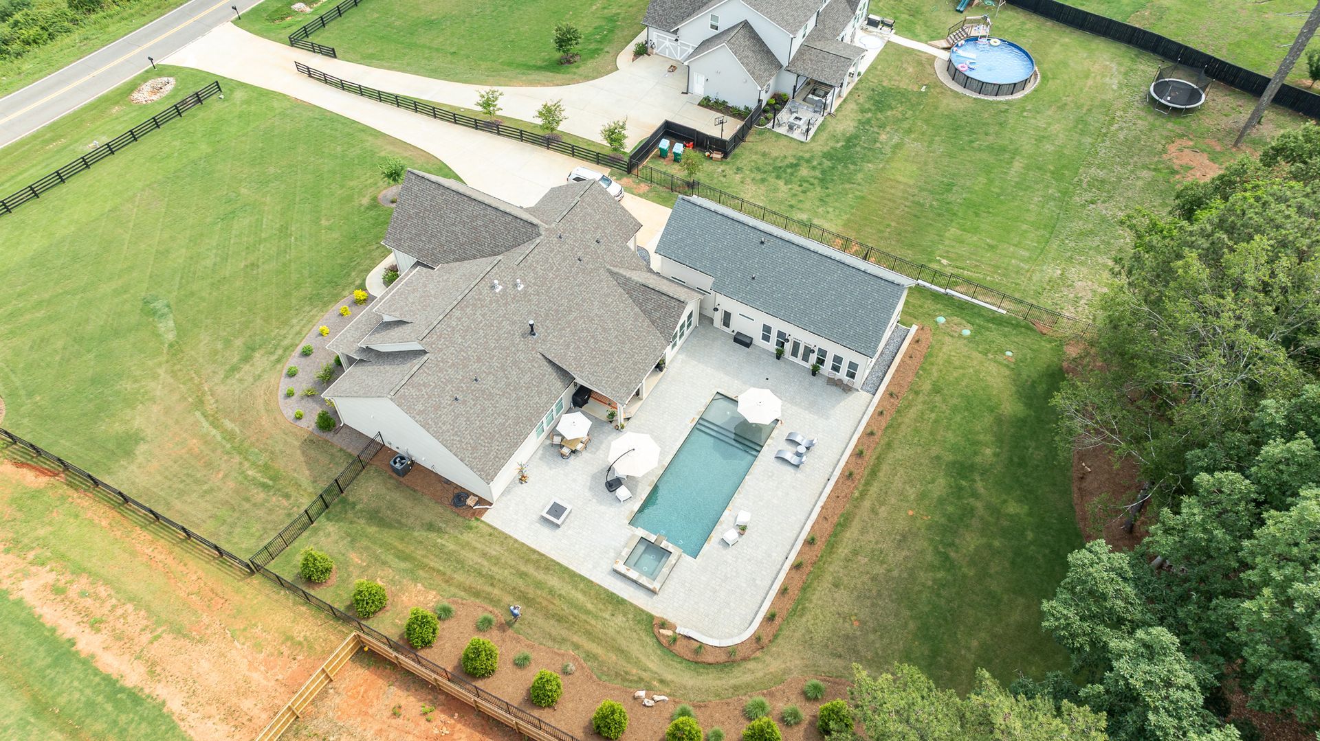 Aerial view of a suburban house with a backyard pool, patio, lawn, and surrounding trees.