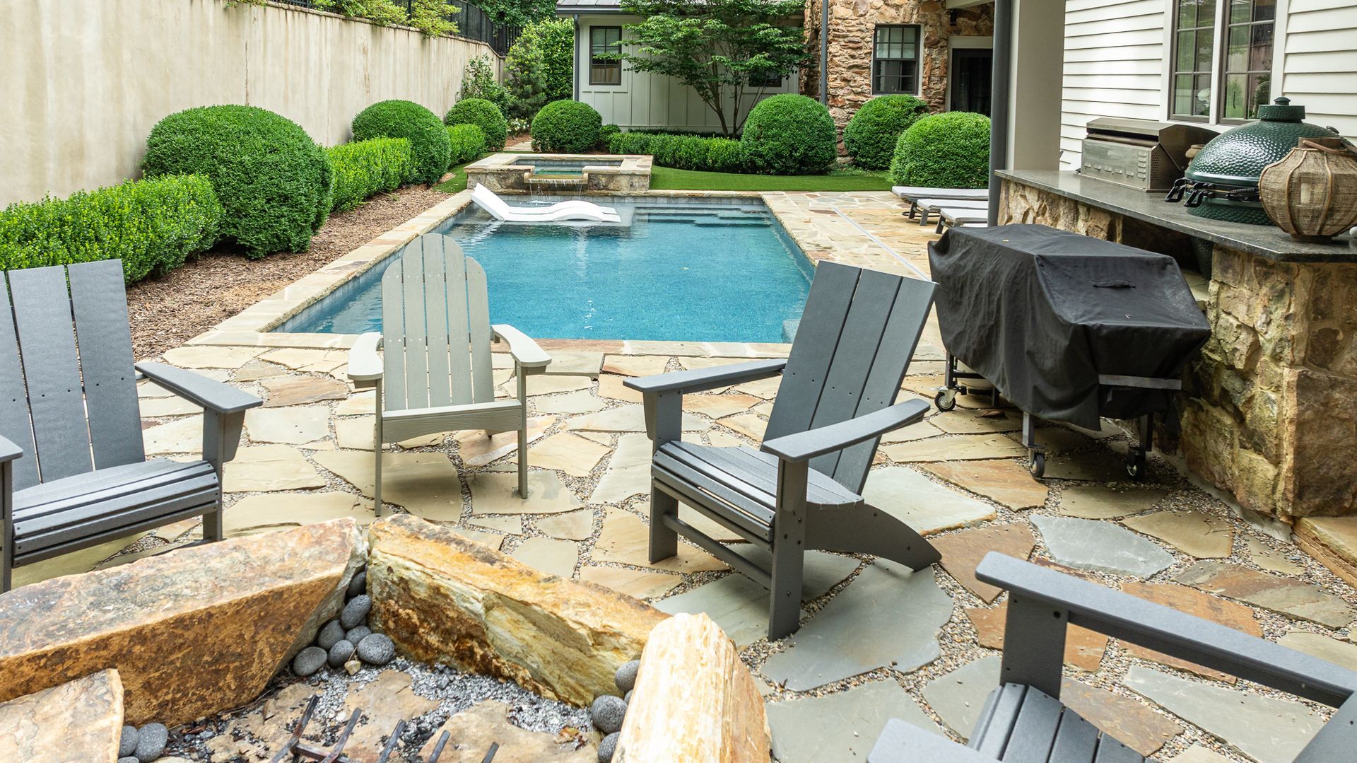 Patio with lounge chairs, a pool, stone pavers, and a covered grill in a landscaped backyard