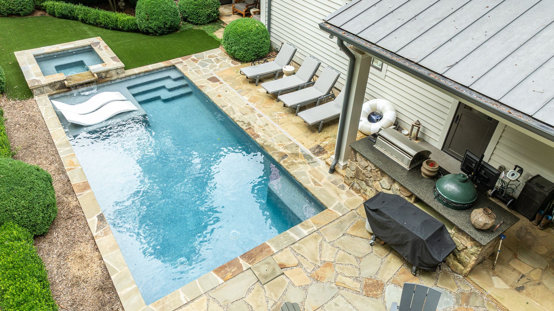 Backyard pool with stone patio, hot tub, lounge chairs, and a covered grill area
