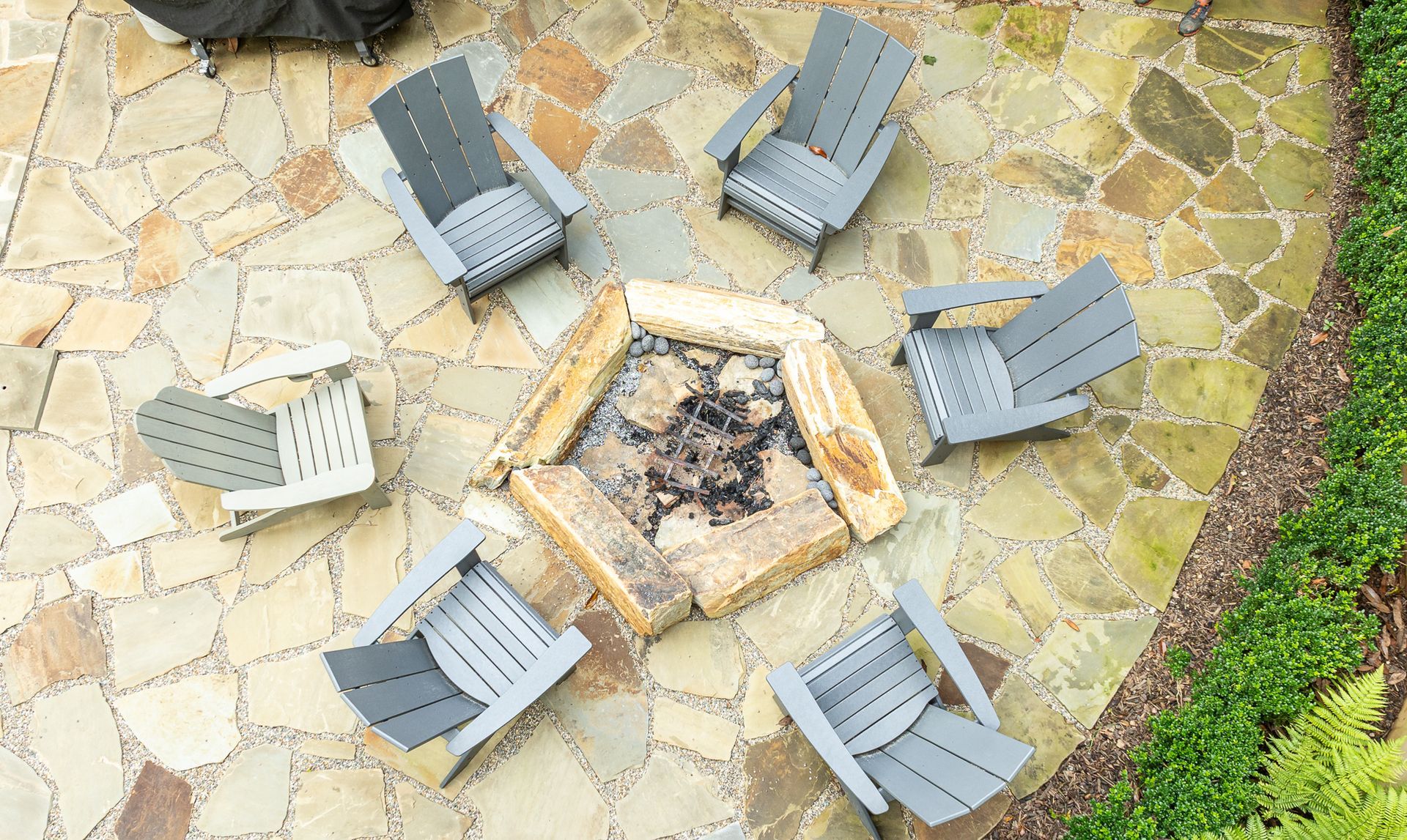 Six gray Adirondack chairs around a hexagonal stone fire pit on a patio area