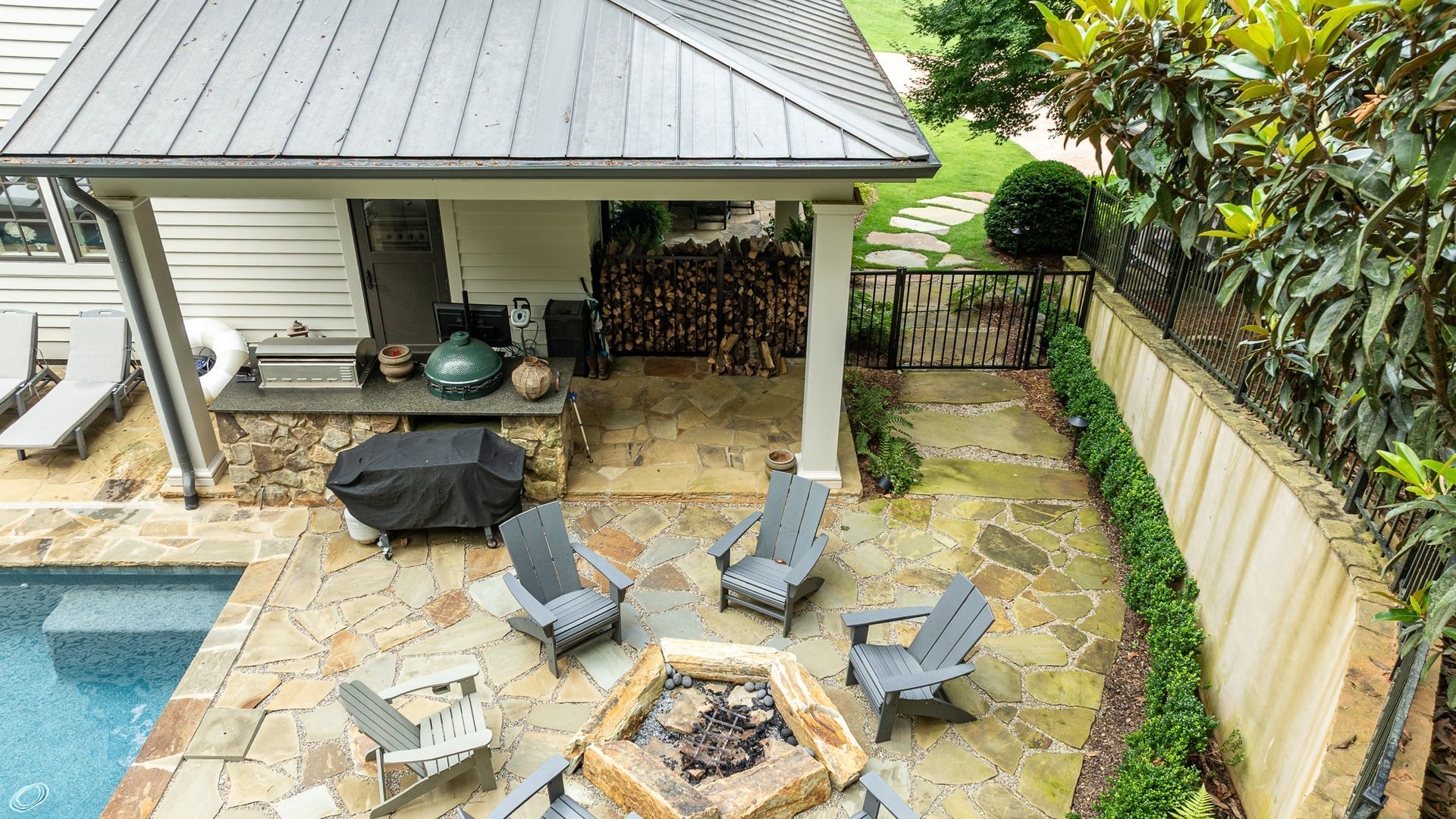 Backyard patio with stone fire pit, gray lounge chairs, covered seating area, and a small pool
