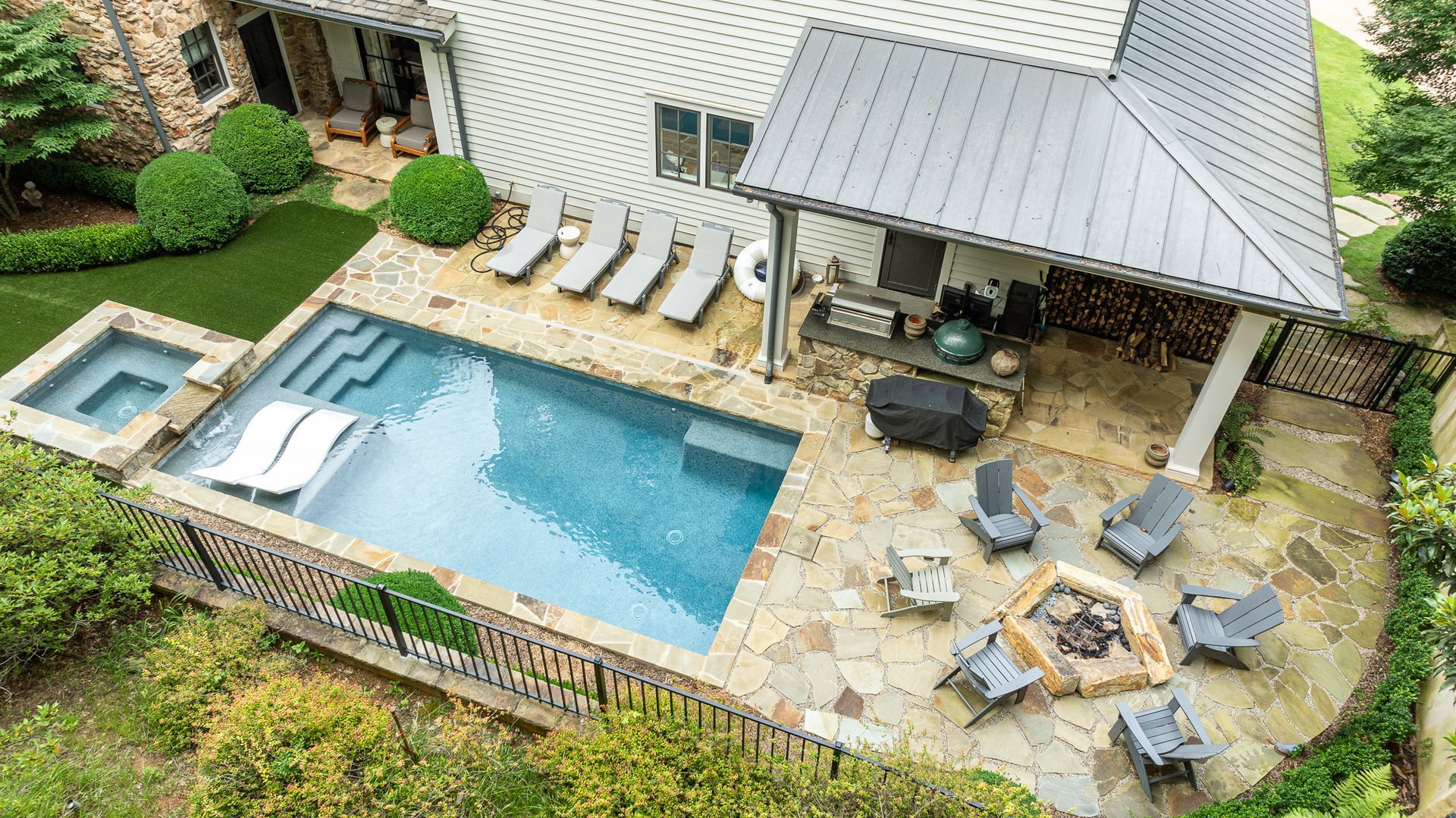 Aerial view of a backyard with a swimming pool, lounge chairs, and a covered patio with seating.