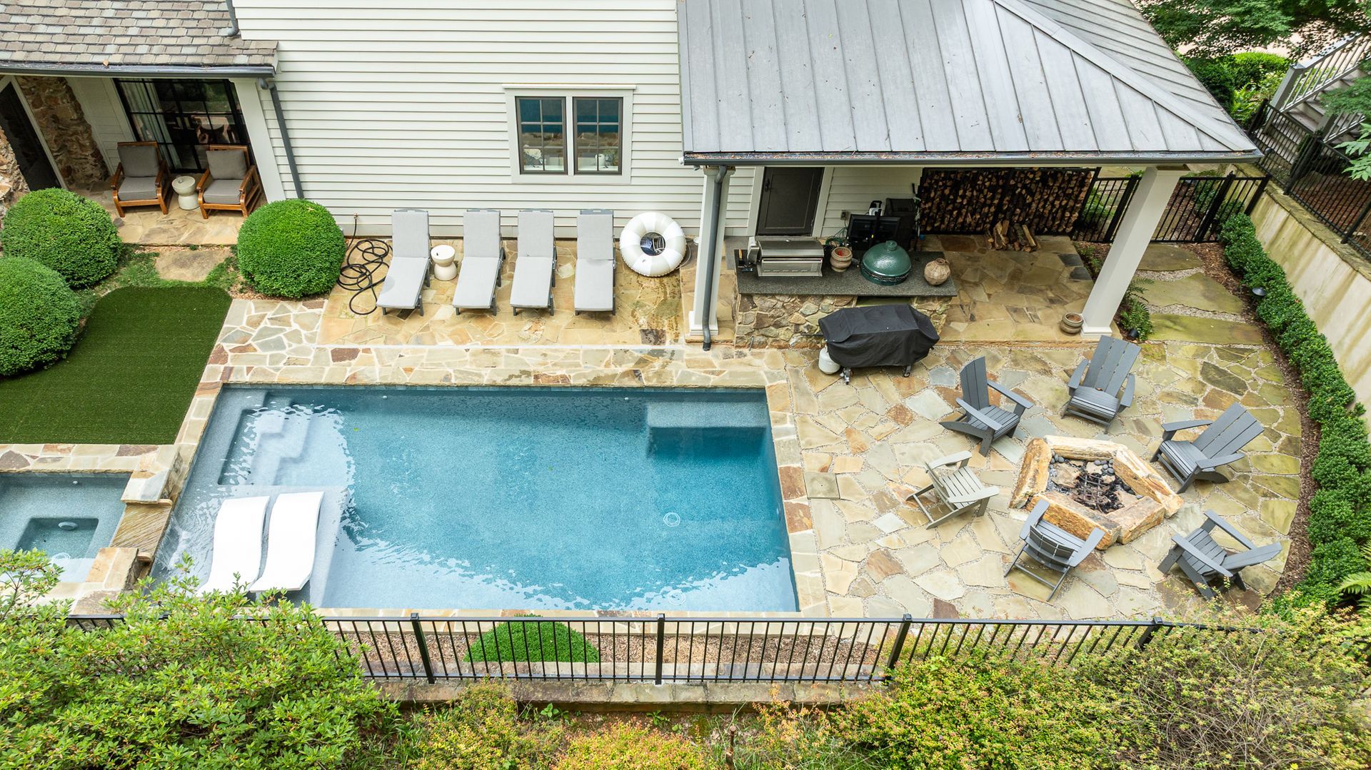 Backyard with a small blue pool, stone patio, lounge chairs, and covered seating area
