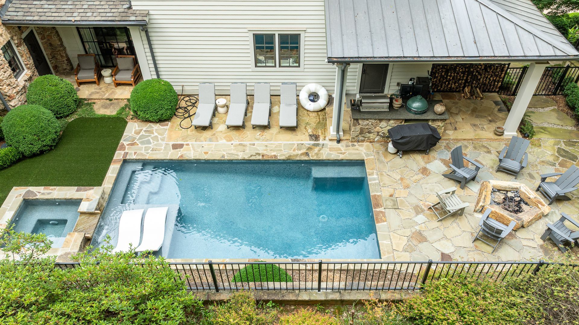 Backyard with a swimming pool, patio seating, covered grill area, and landscaped lawn.