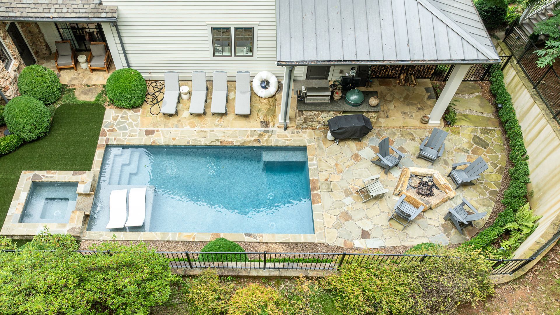 Aerial view of a backyard pool, patio seating area, lounge chairs, and a covered outdoor seating space.