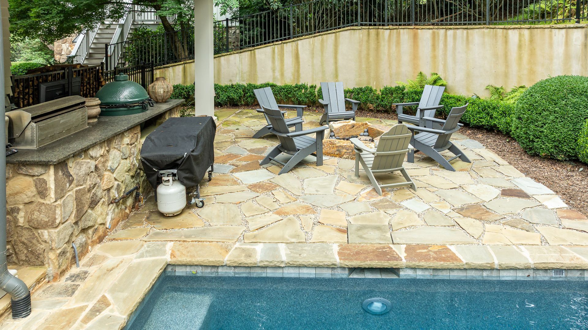 Backyard patio with lounge chairs, stone grill area, and a swimming pool edge