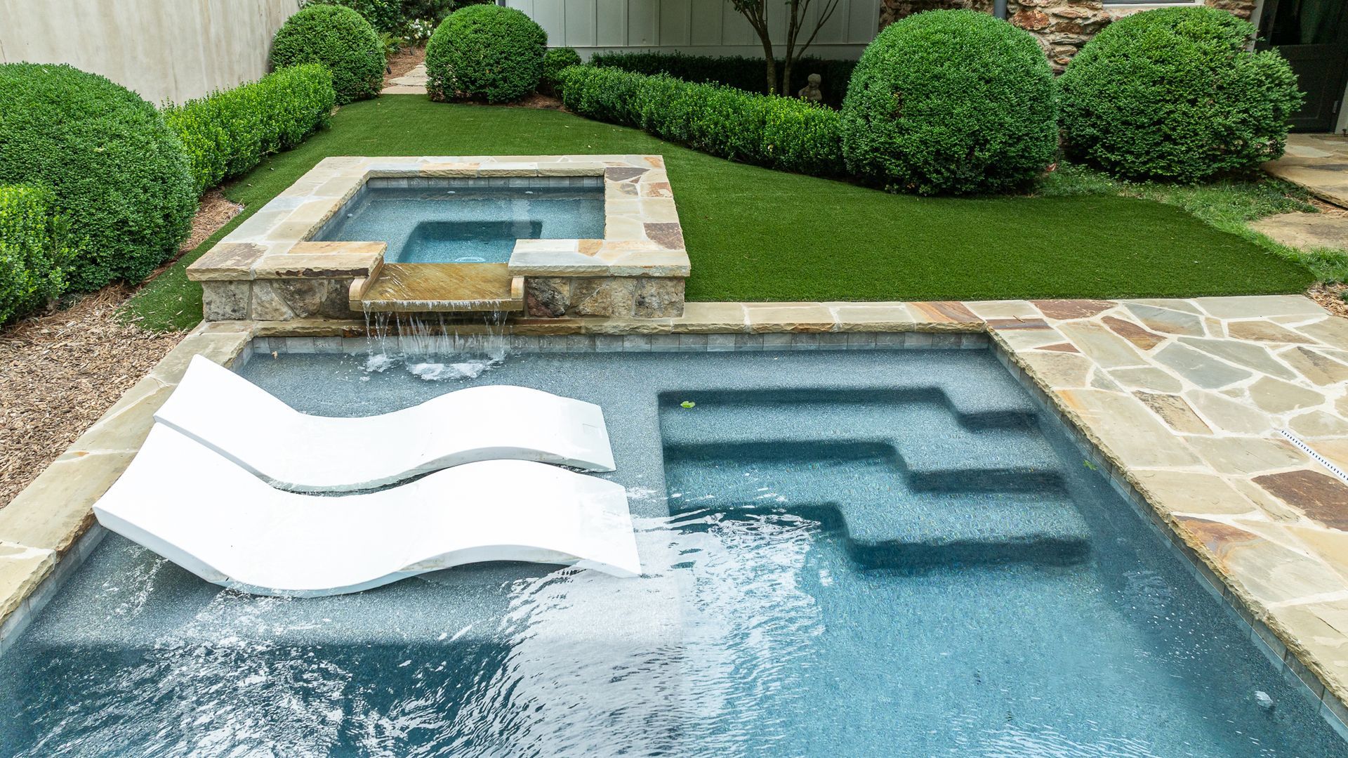 Backyard pool with stone deck, green lawn, and a white floating lounger in the water