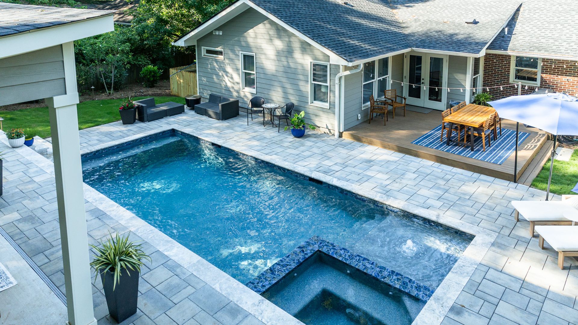 Modern backyard with rectangular swimming pool, spa, stone patio, and house deck with outdoor seating