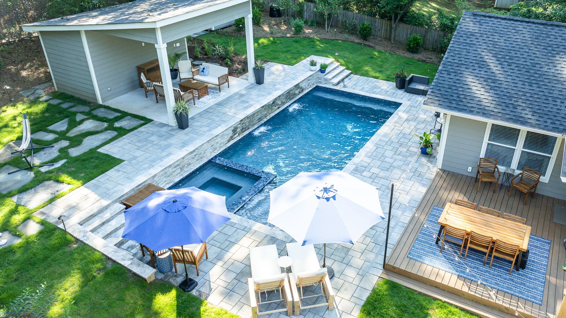Aerial view of a backyard pool with lounge chairs, umbrellas, and two covered patios