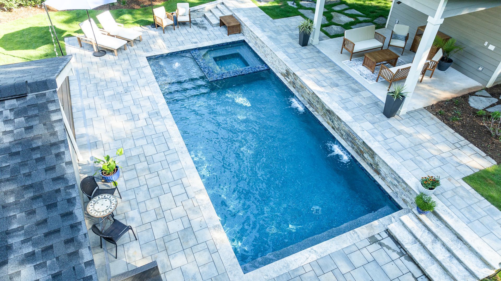 Overhead view of a rectangular blue swimming pool with stone patio and lounge chairs surrounding it