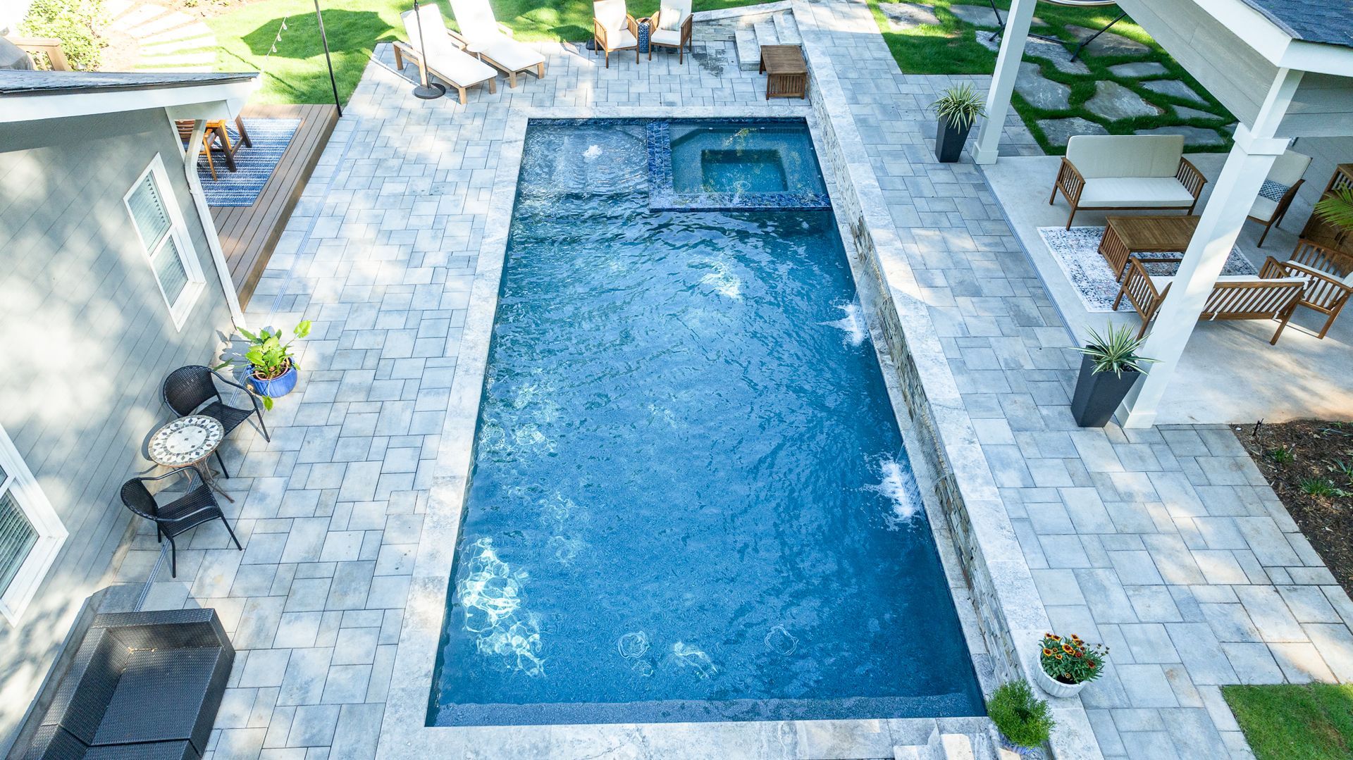 Rectangular backyard pool with blue water, stone patio, and lounge chairs under a pergola