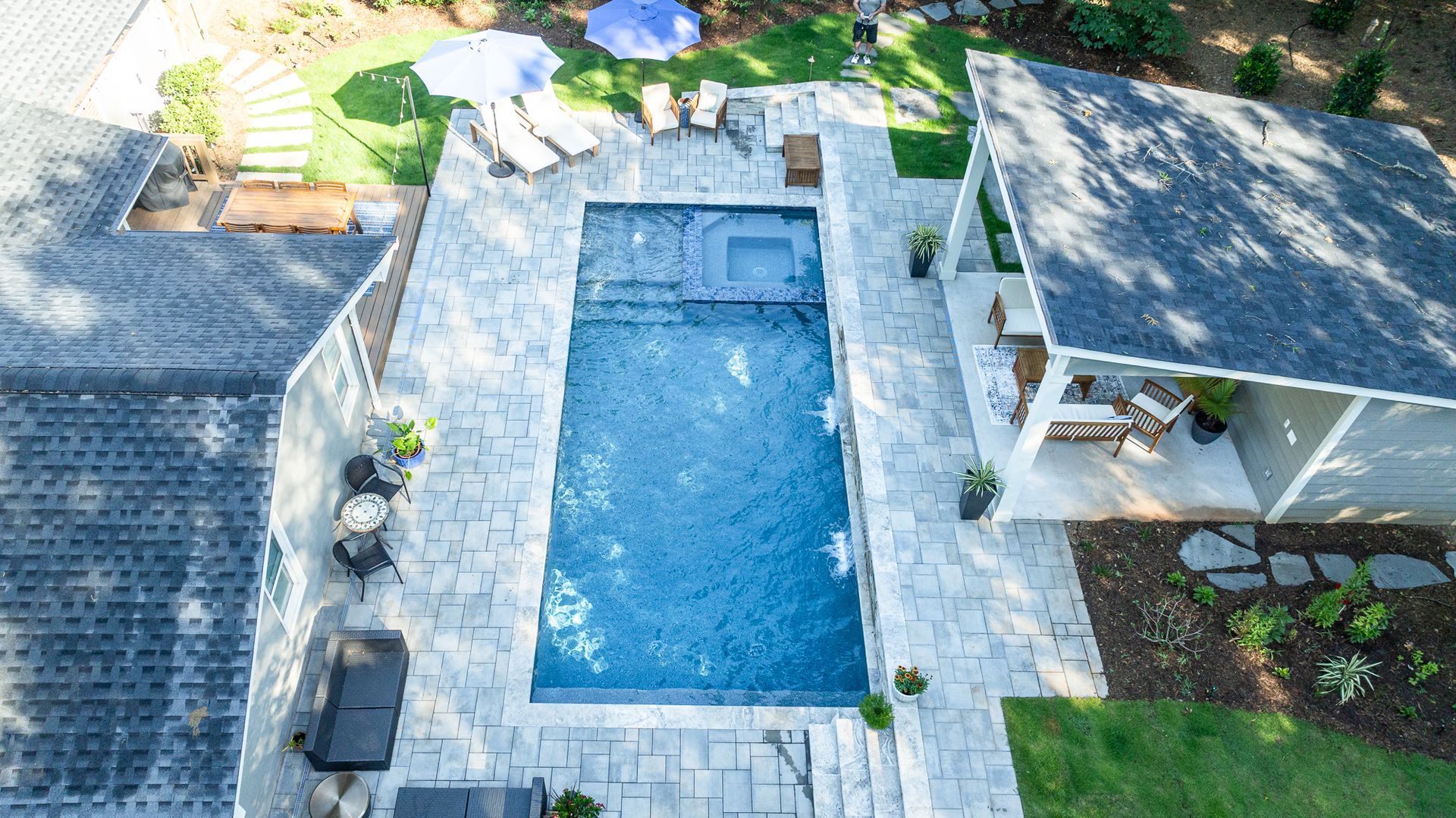 Aerial view of a rectangular backyard pool with patio, lounge chairs, and a shaded seating area.