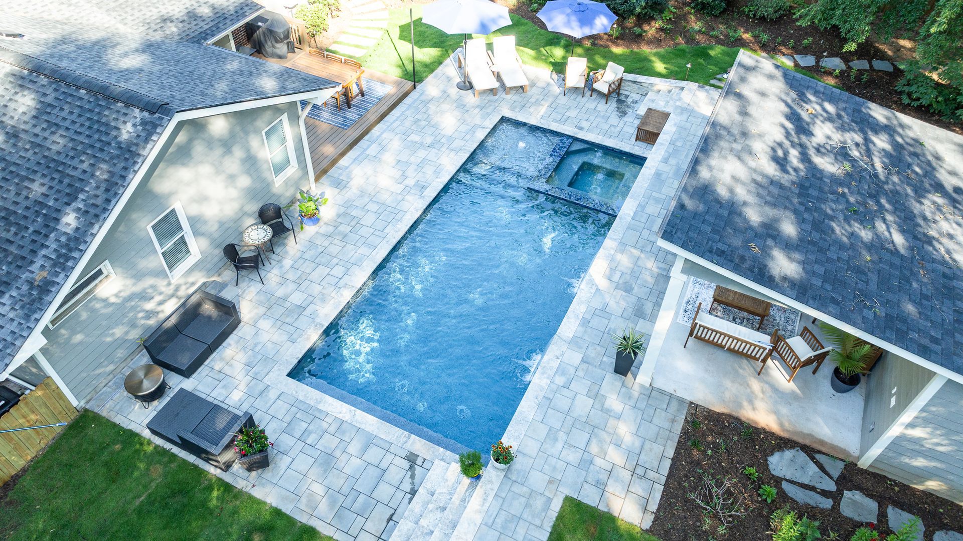 Aerial view of a backyard with a rectangular swimming pool, patio seating, and a small shed.