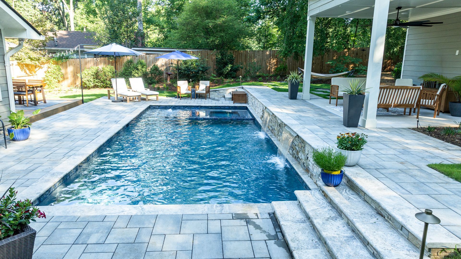 Backyard patio with a rectangular swimming pool, stone deck, lounge chairs, and a covered seating area