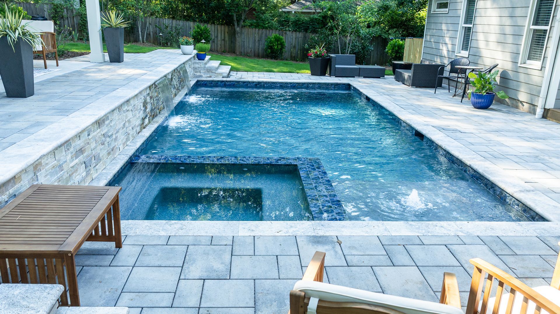 Modern backyard with a rectangular blue-tiled pool and patio seating on a stone deck