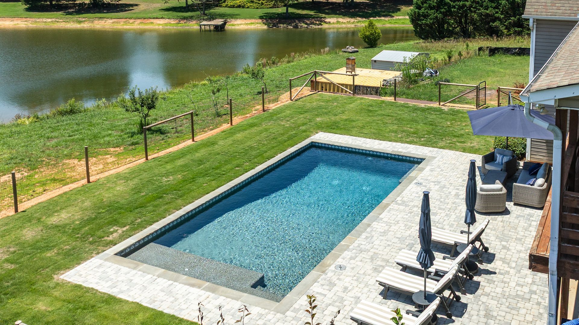 Backyard with rectangular pool, lounge chairs, patio, and lake view under bright sunlight