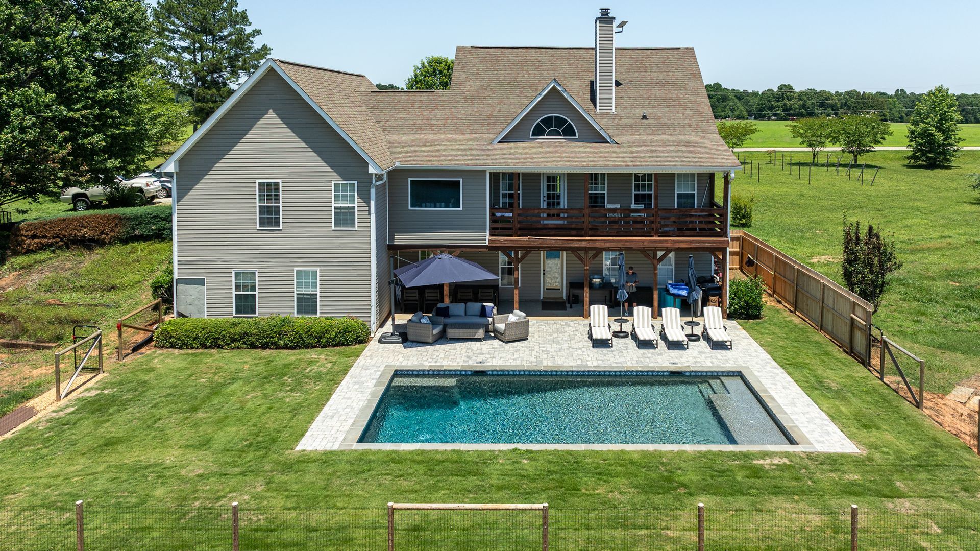 Backyard house with a swimming pool, lounge chairs, and a covered patio on a sunny day