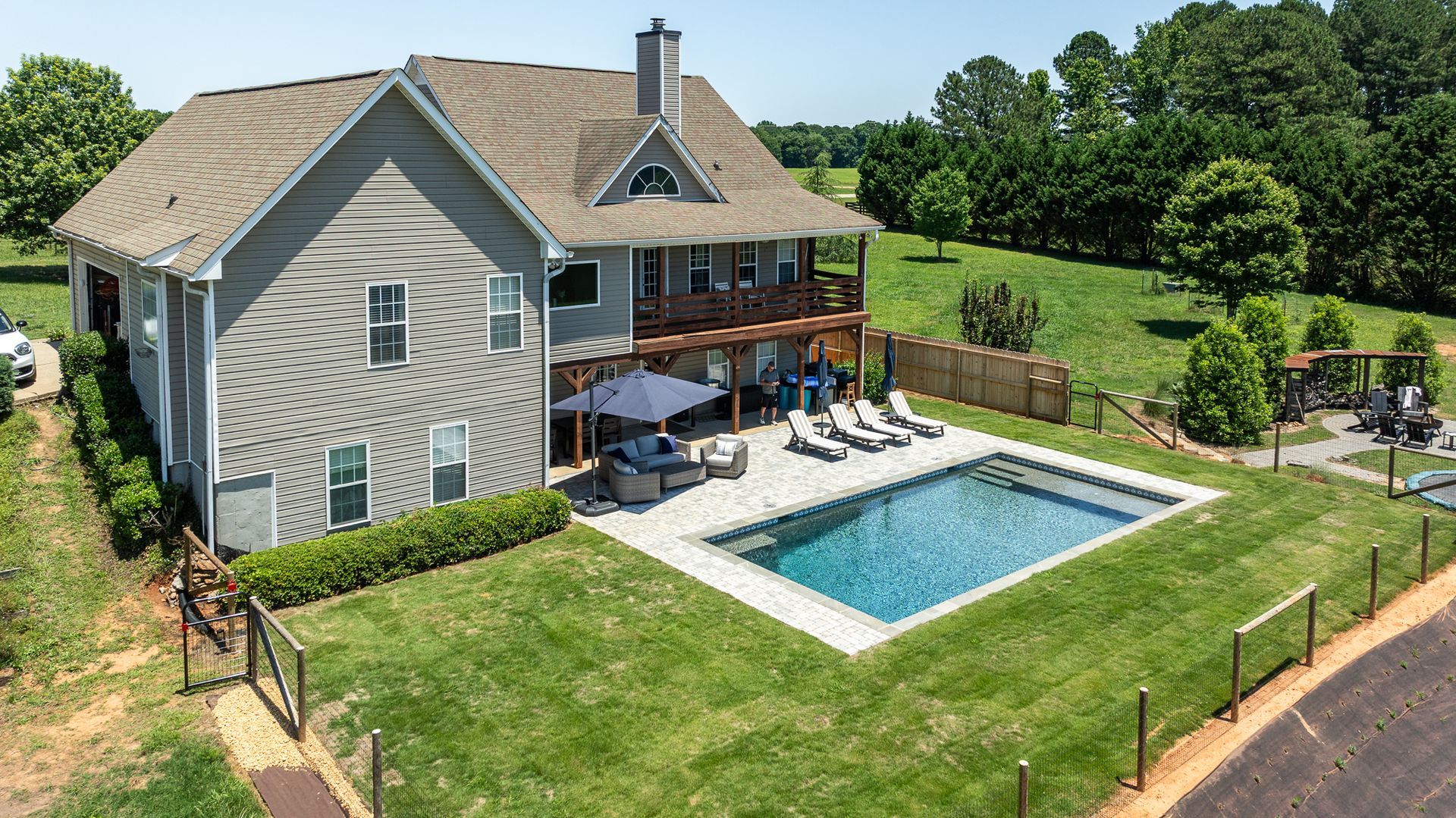 Aerial view of a gray house with a backyard deck, patio seating, and a rectangular swimming pool.
