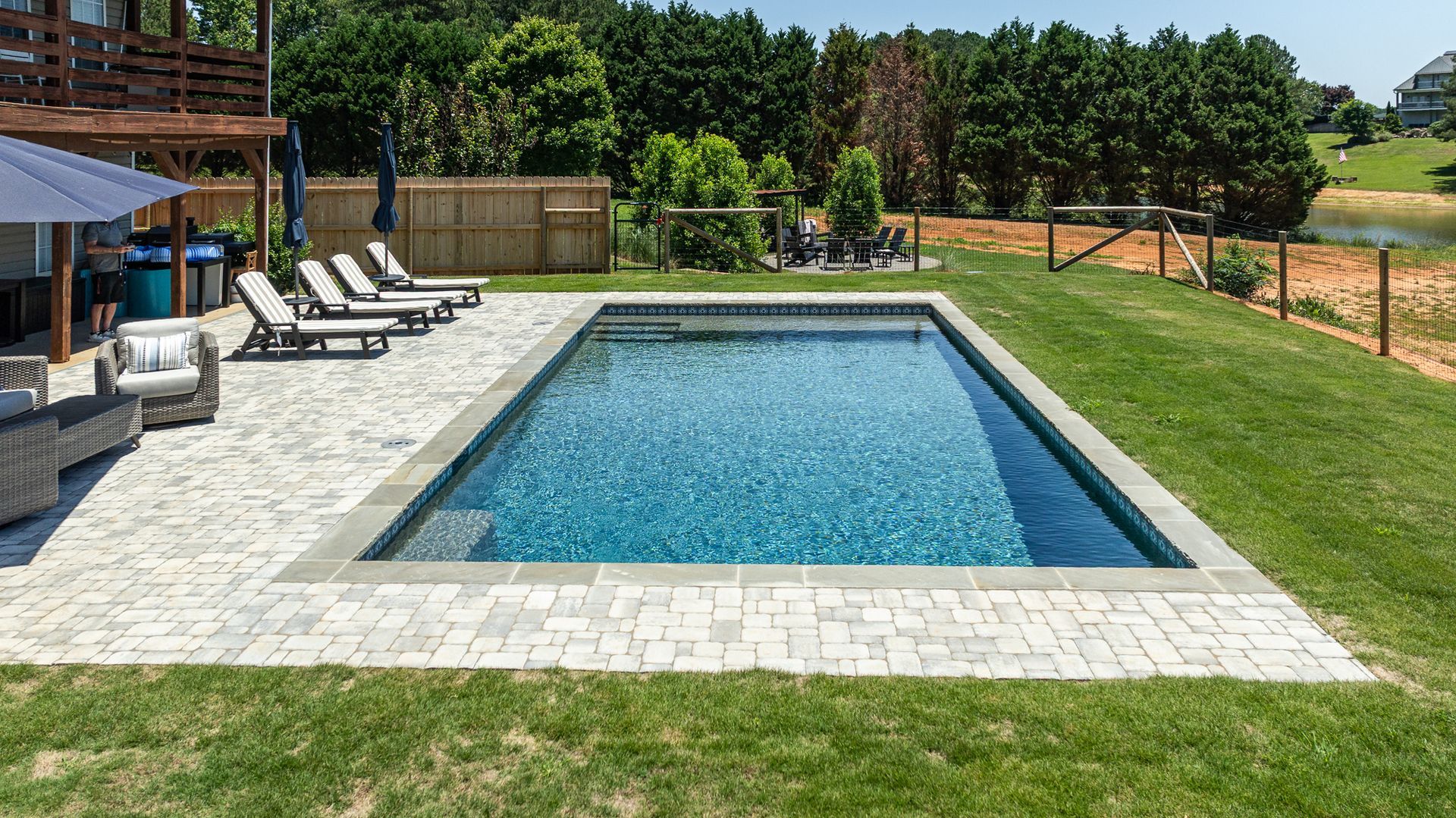 Backyard swimming pool with lounge chairs, green lawn, and a wooden fence