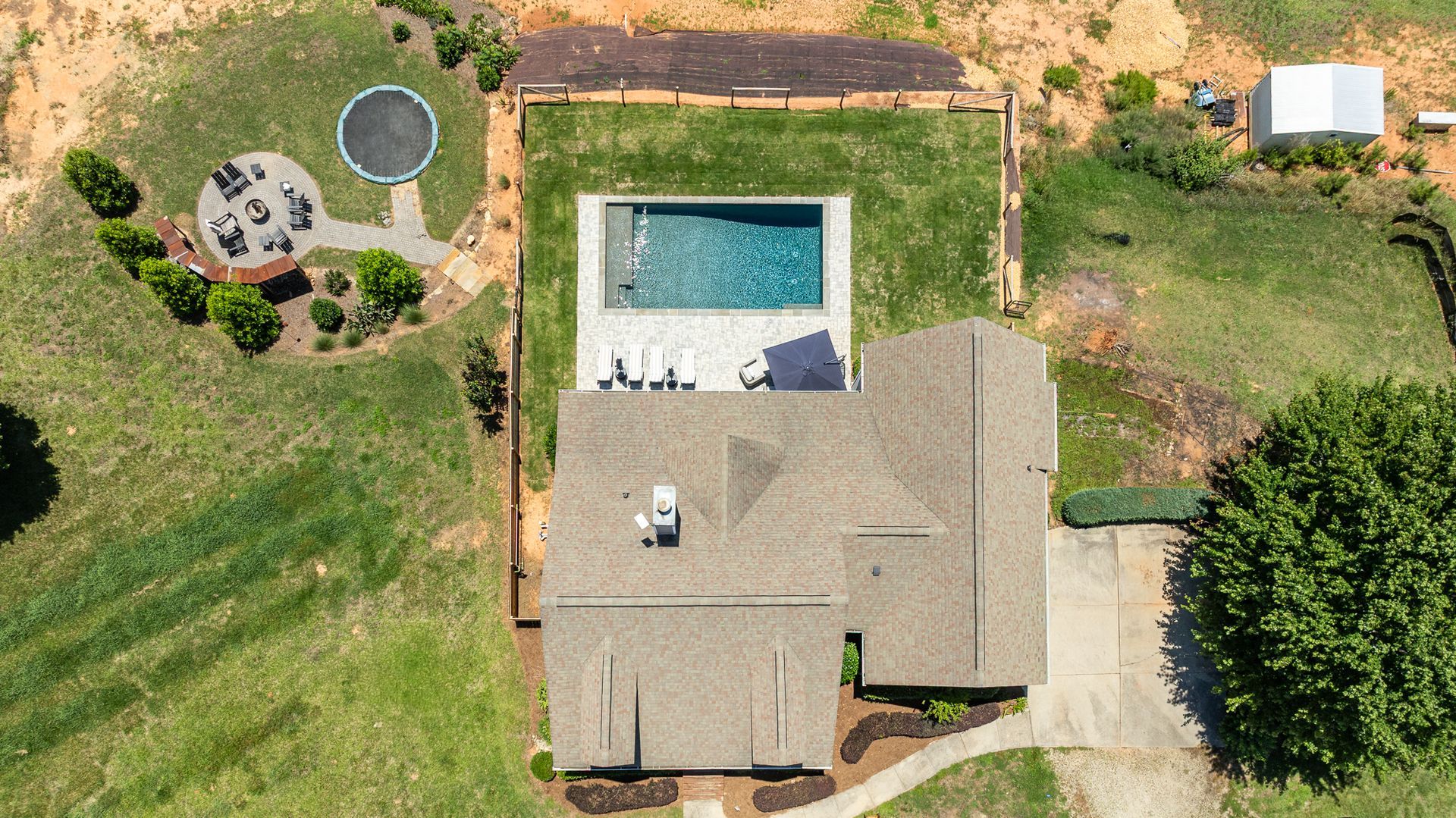 Aerial view of a house with a backyard pool, patio, lawn, and trees