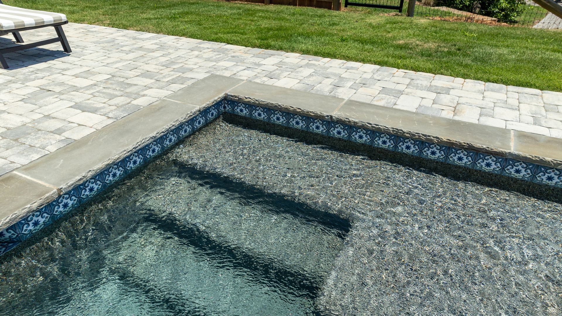Backyard swimming pool with clear water, stone deck, and a bench nearby