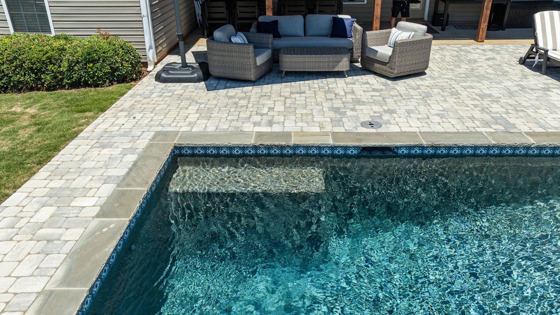Backyard pool beside a paved patio with outdoor seating and cushioned chairs under shade