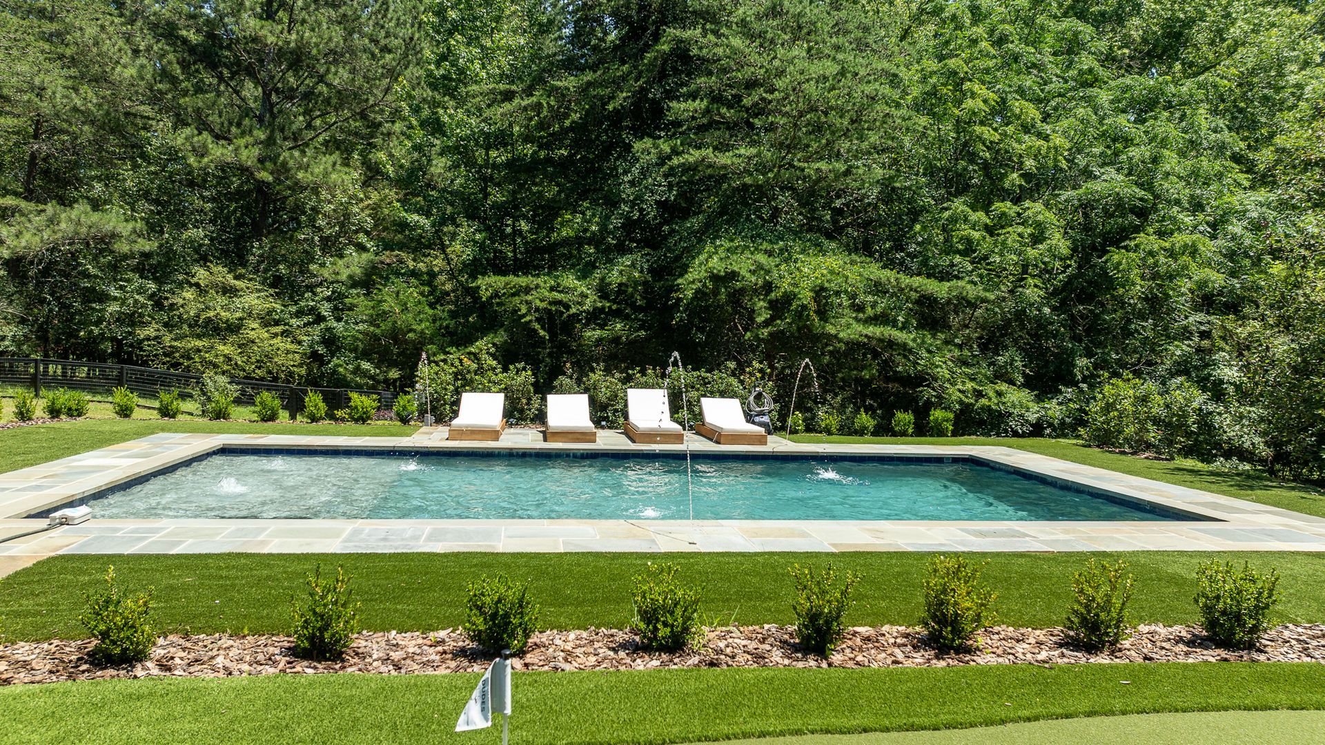 Rectangular backyard swimming pool with lounge chairs, bordered by grass and trees