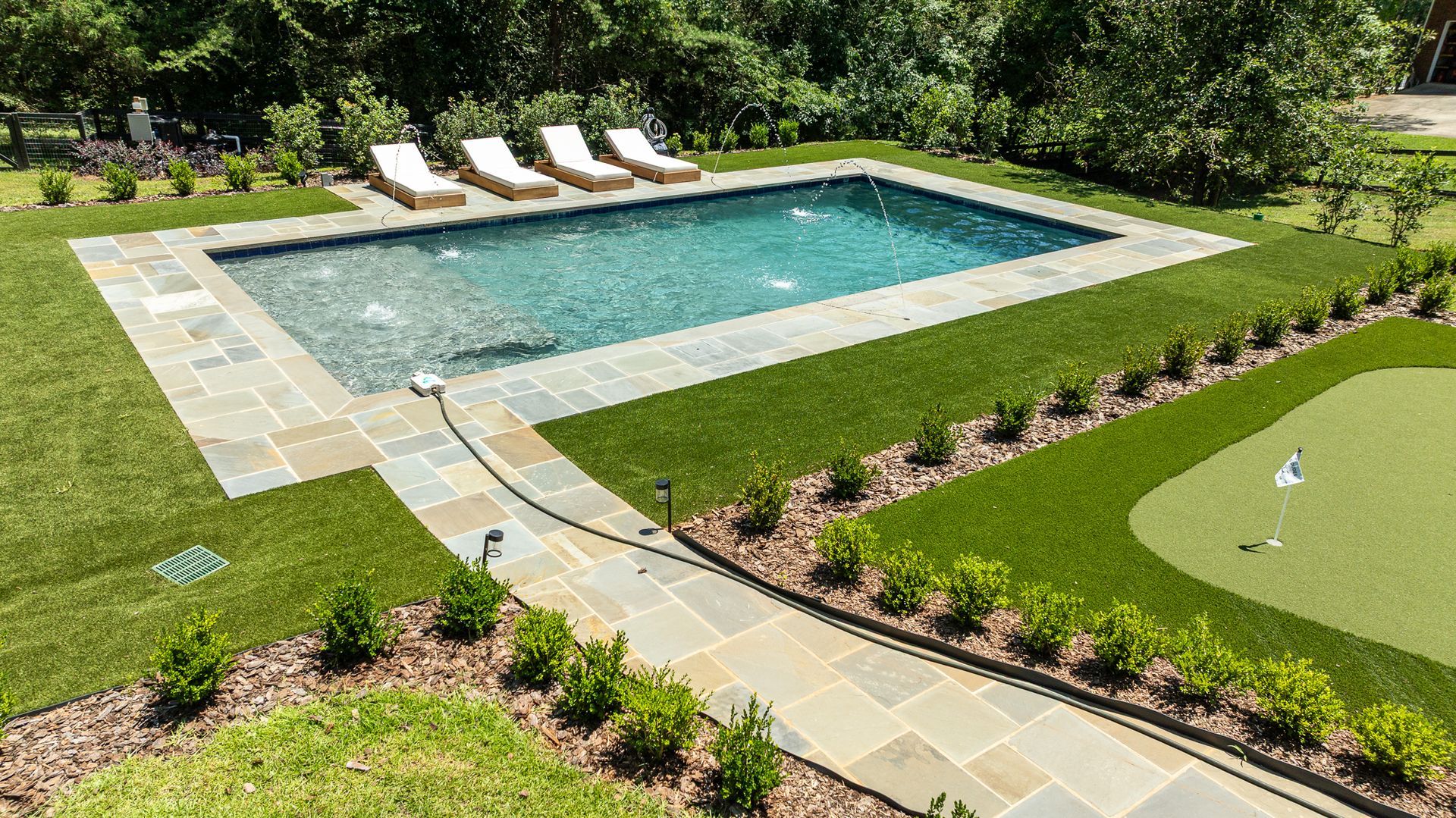 Backyard pool with lounge chairs, stone patio, lush lawn, and a putting green