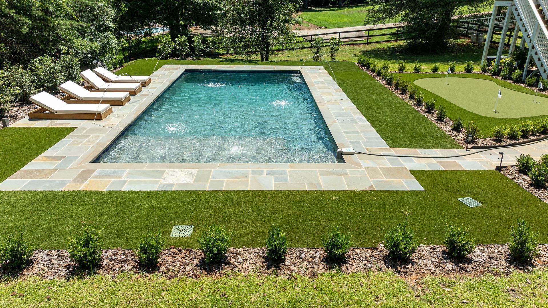 Rectangular backyard pool with lounge chairs, green lawn, and landscaped garden